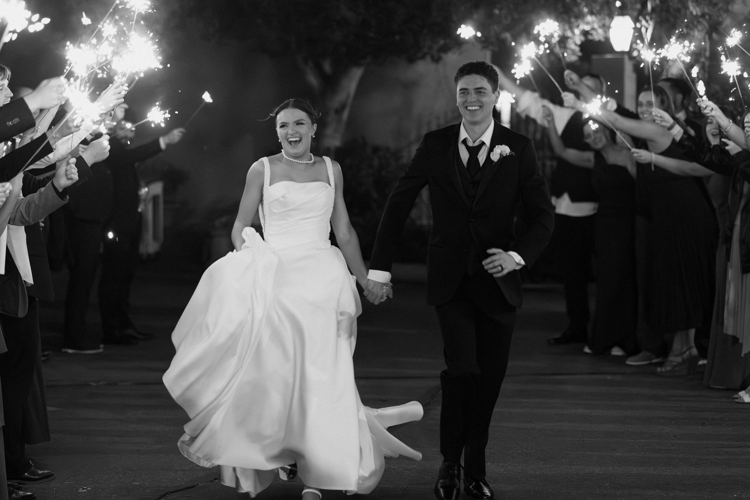 Black and white photo of bride and groom walking through sparkler sendoff.