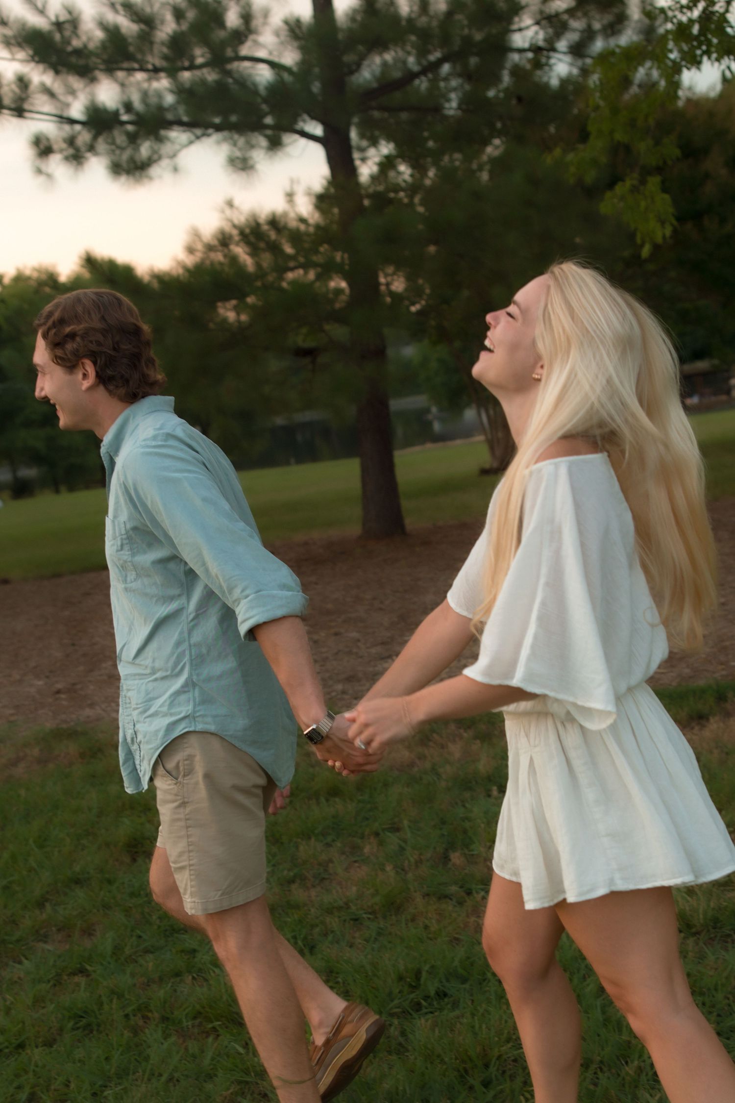 Joyful blonde woman laughing while holding hands with her partner in a park.