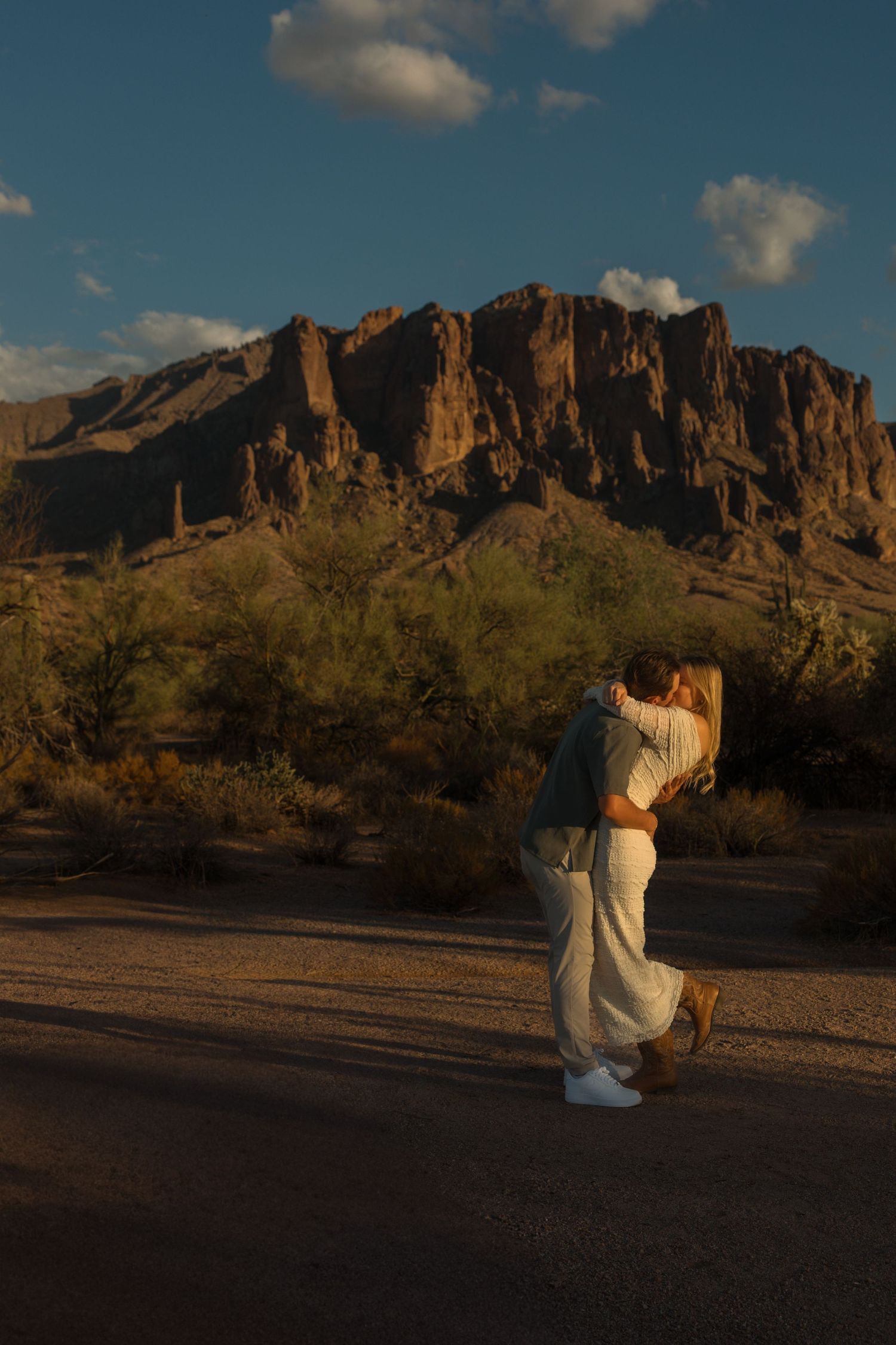 Couple kissing at golden hour in front of Superstition Mountains in Arizona desert landscape.