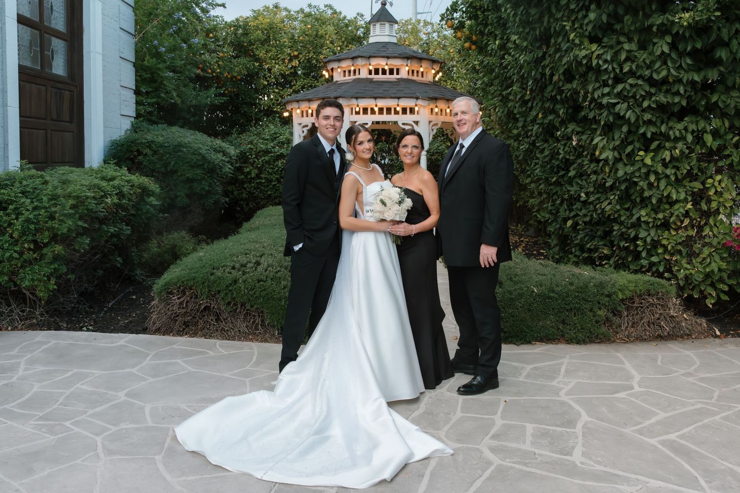 Bride and groom pose with two guests outside an elegant wedding venue at night.