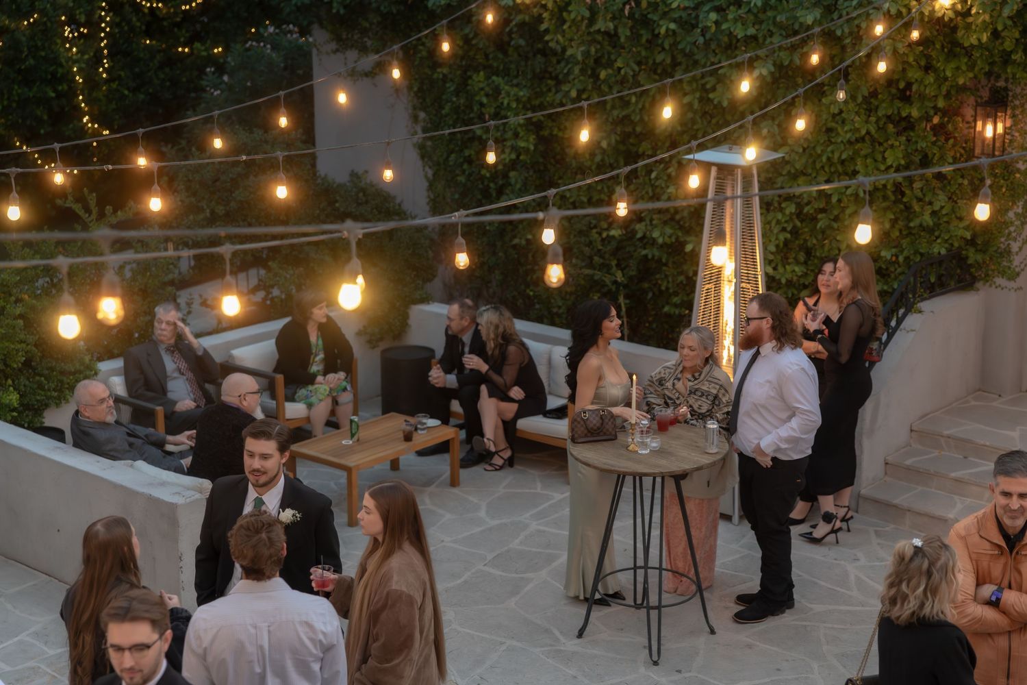 Guests mingle at an outdoor evening wedding reception under warm string lights on a patio.