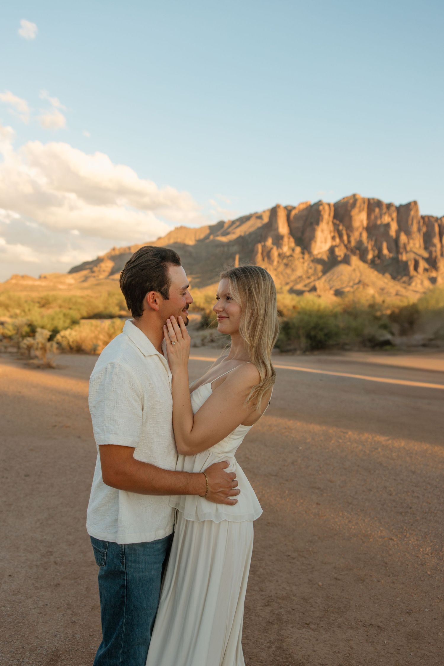 Couple embracing at golden hour with Superstition Mountains in the Arizona desert background.