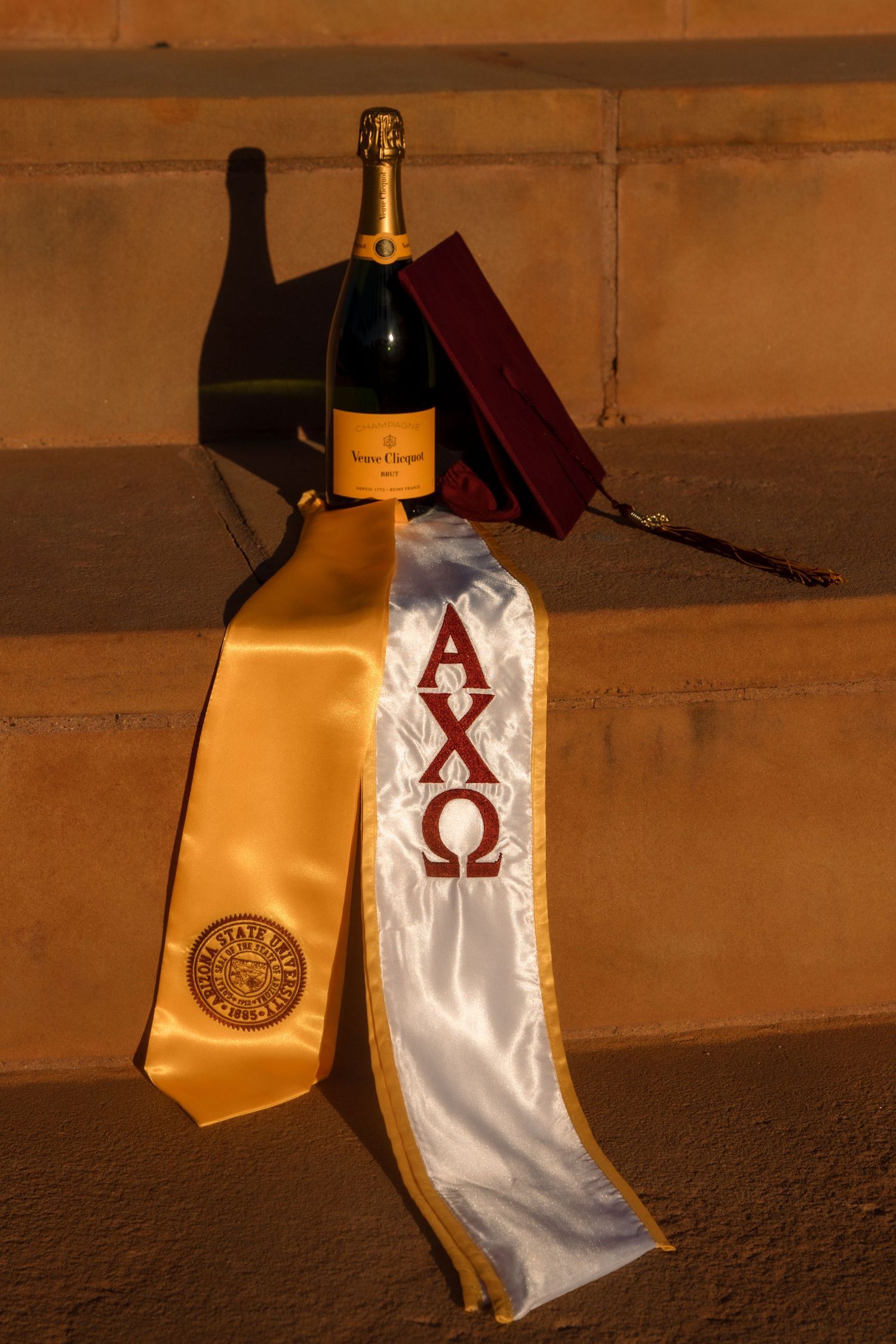 Alpha Chi Omega sorority graduation sash with gold ASU stole and Veuve Clicquot champagne bottle.