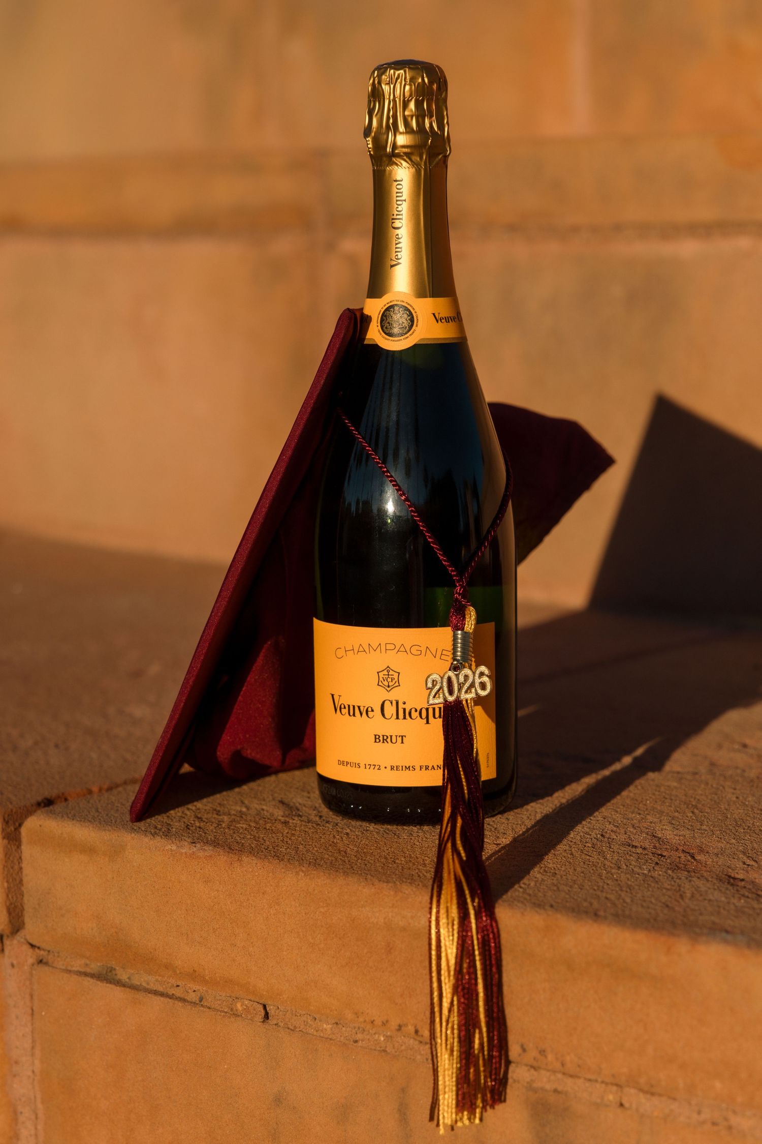 Veuve Clicquot champagne bottle with maroon graduation cap and tassel on stone ledge, 2026.