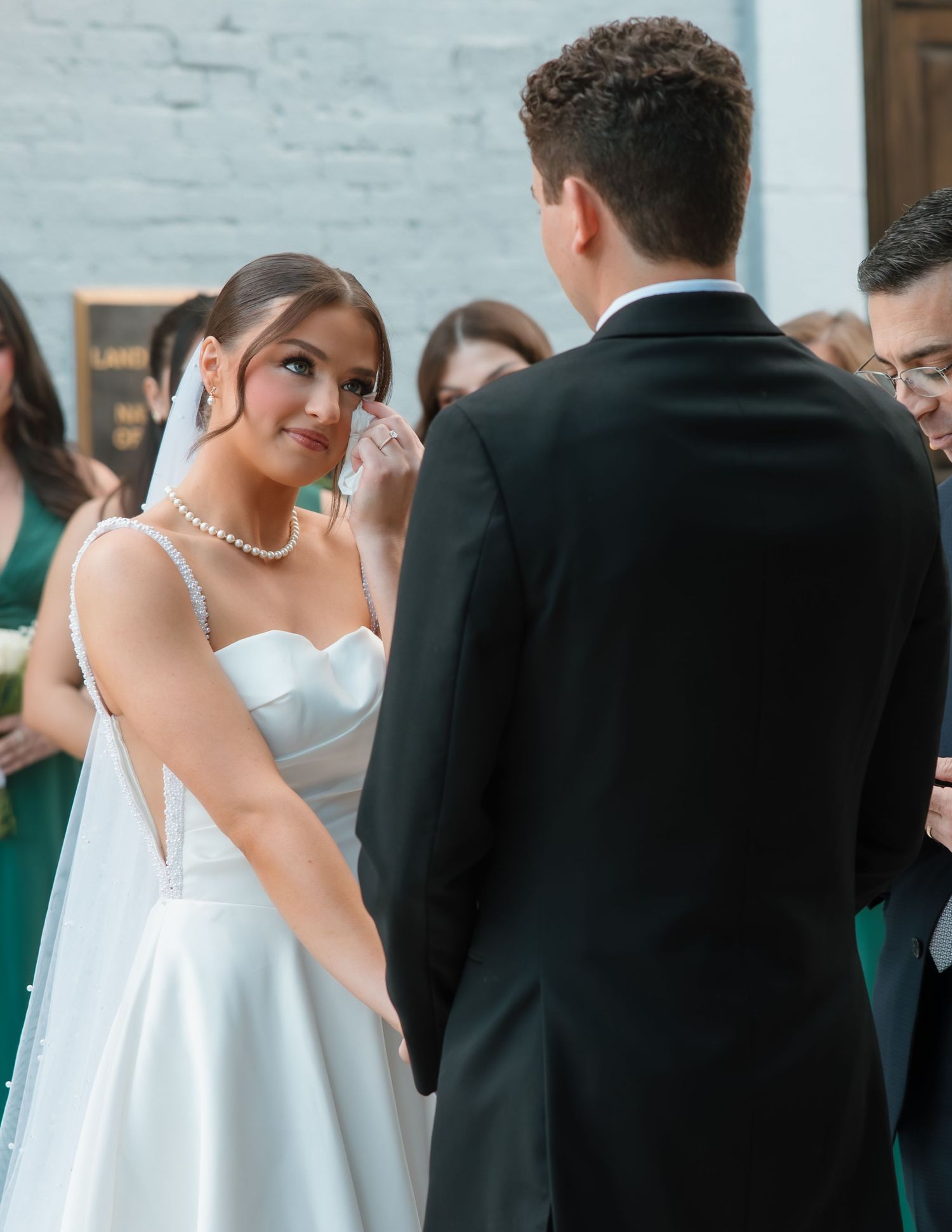 Emotional bride in white gown wiping tears during outdoor wedding ceremony with groom.