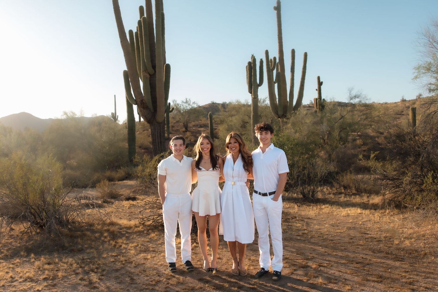 Family of four in white outfits standing together in desert landscape with tall saguaro cacti.