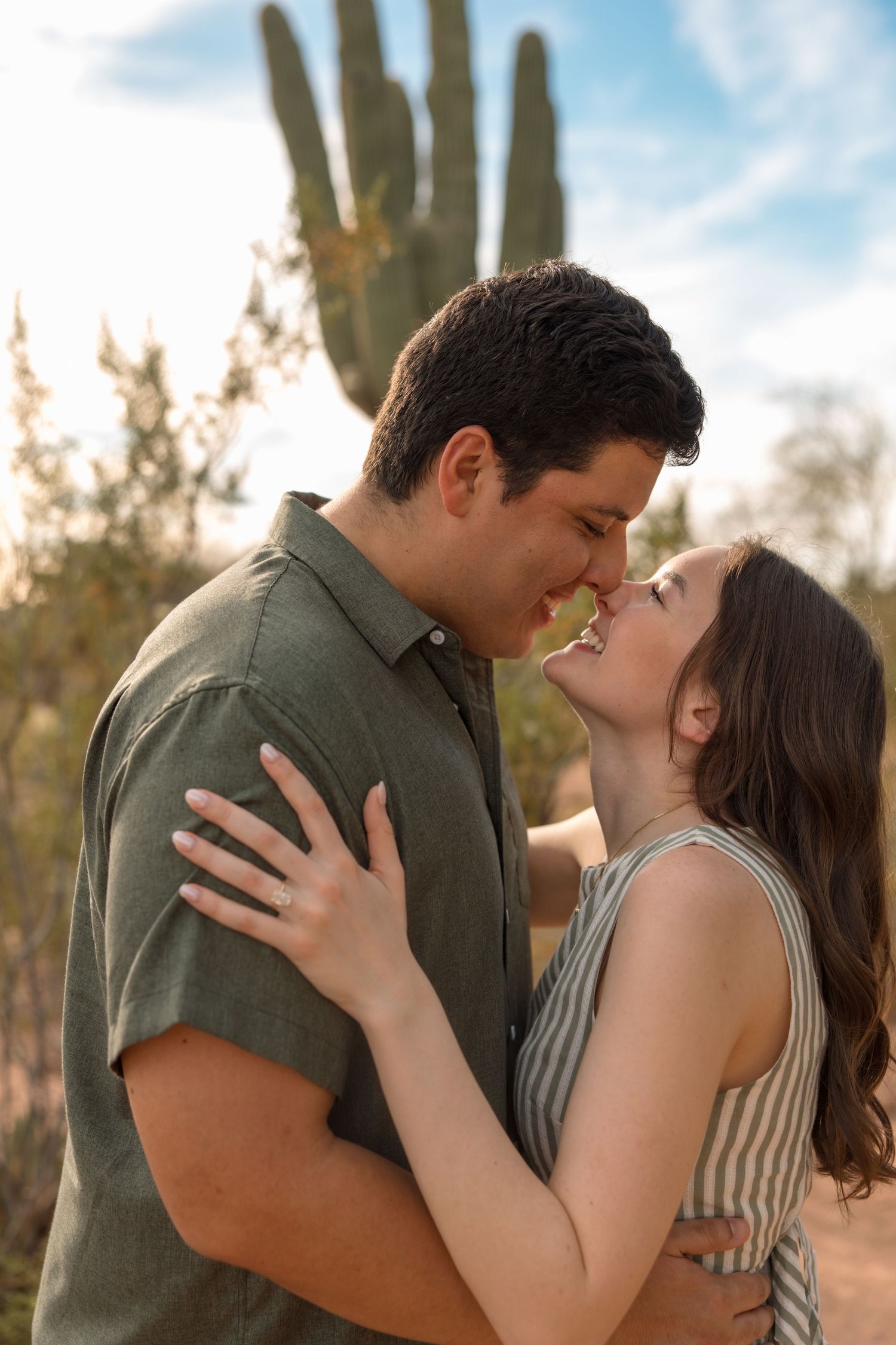 A happy couple sharing a tender almost-kiss moment with a saguaro cactus in the Arizona desert background.