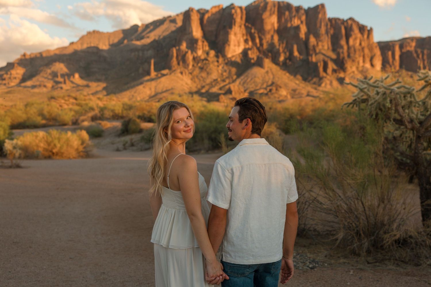 Couple holding hands at sunset with Superstition Mountains in Arizona desert background.