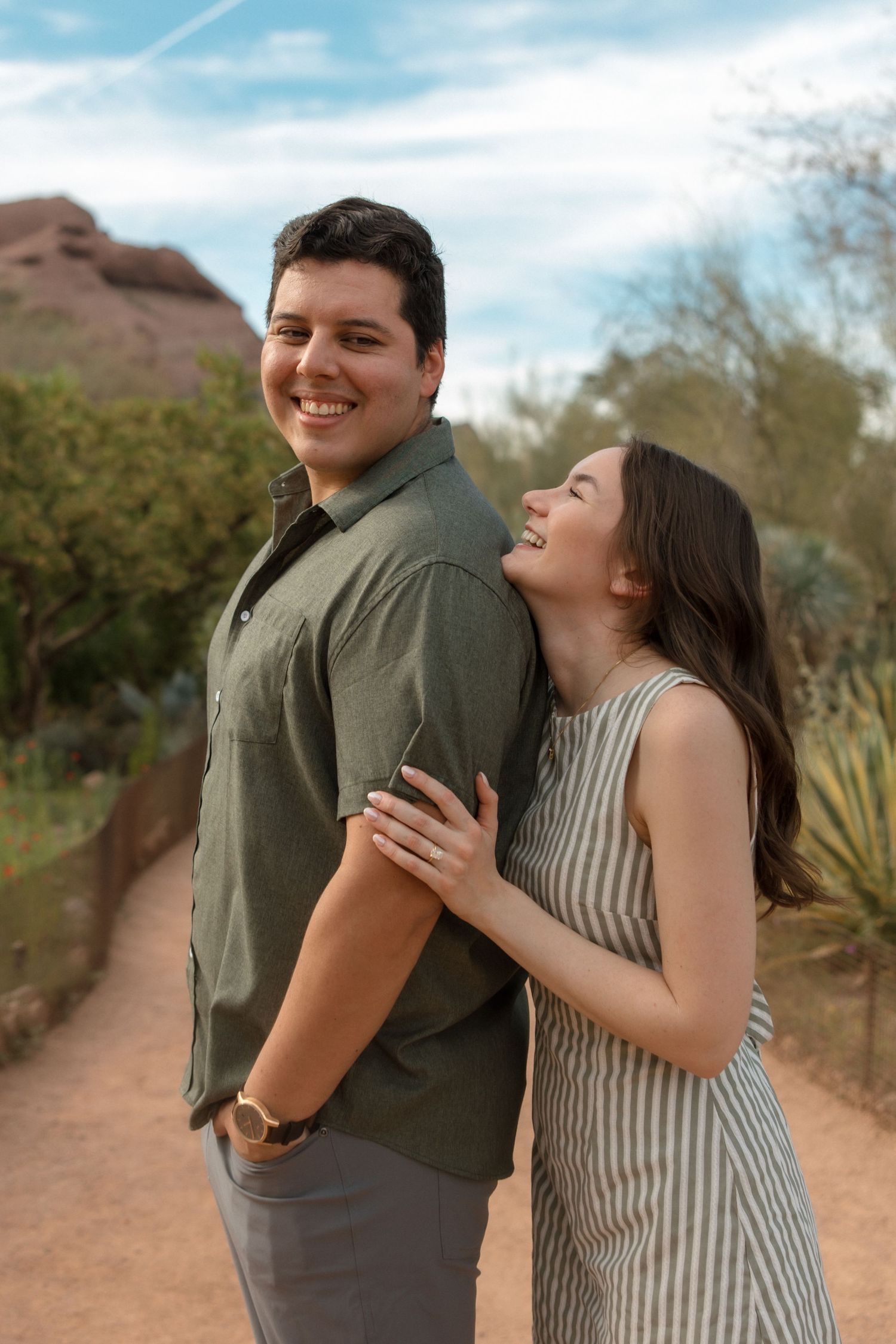 Joyful engaged couple laughing together on a desert garden path with red rock formations.