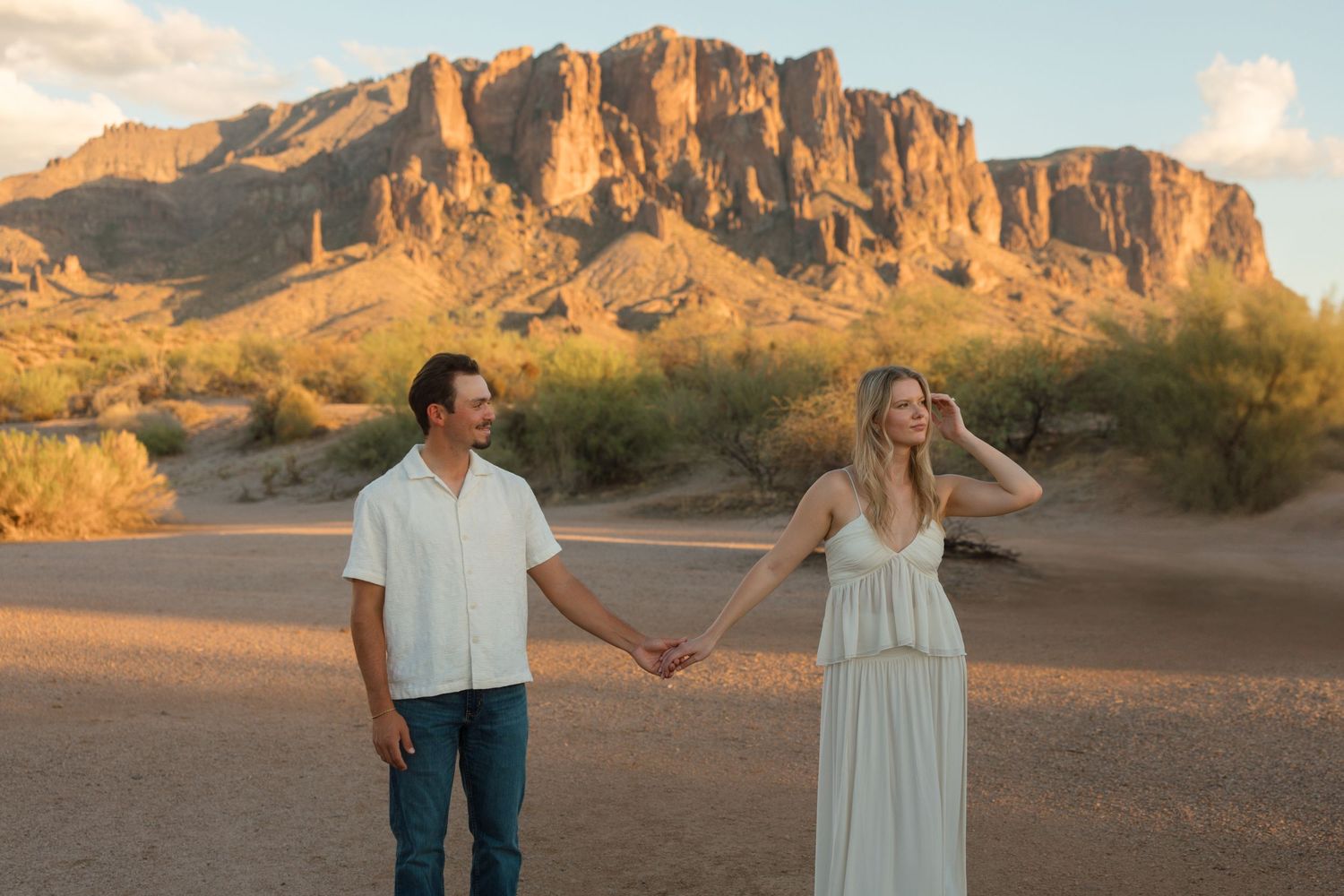 Couple holding hands in Arizona desert with stunning Superstition Mountains backdrop at sunset.