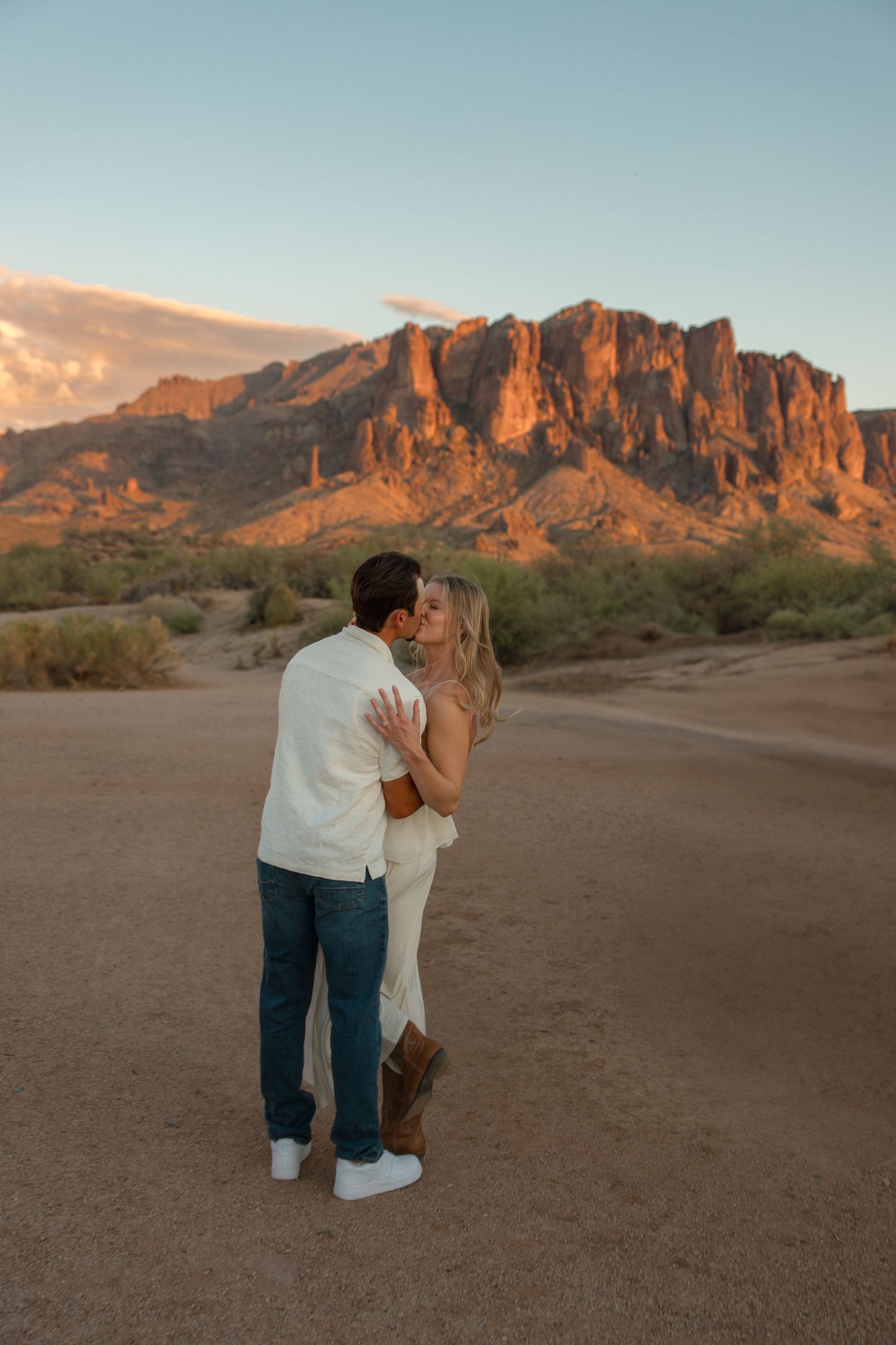 Couple sharing a romantic kiss at golden hour with the Superstition Mountains glowing in the Arizona desert backdrop.