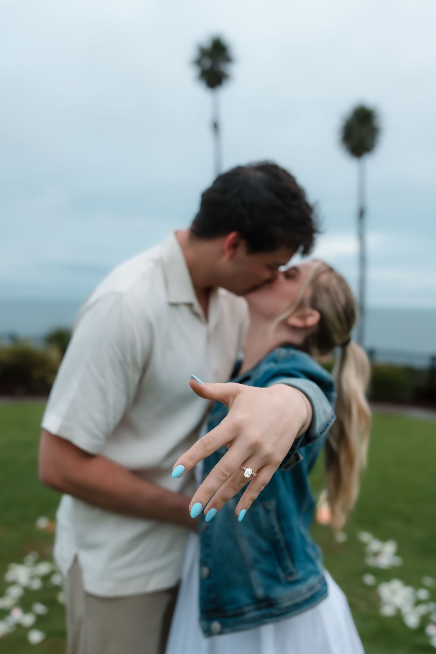 Engaged couple kissing while woman shows off diamond engagement ring with teal nails.
