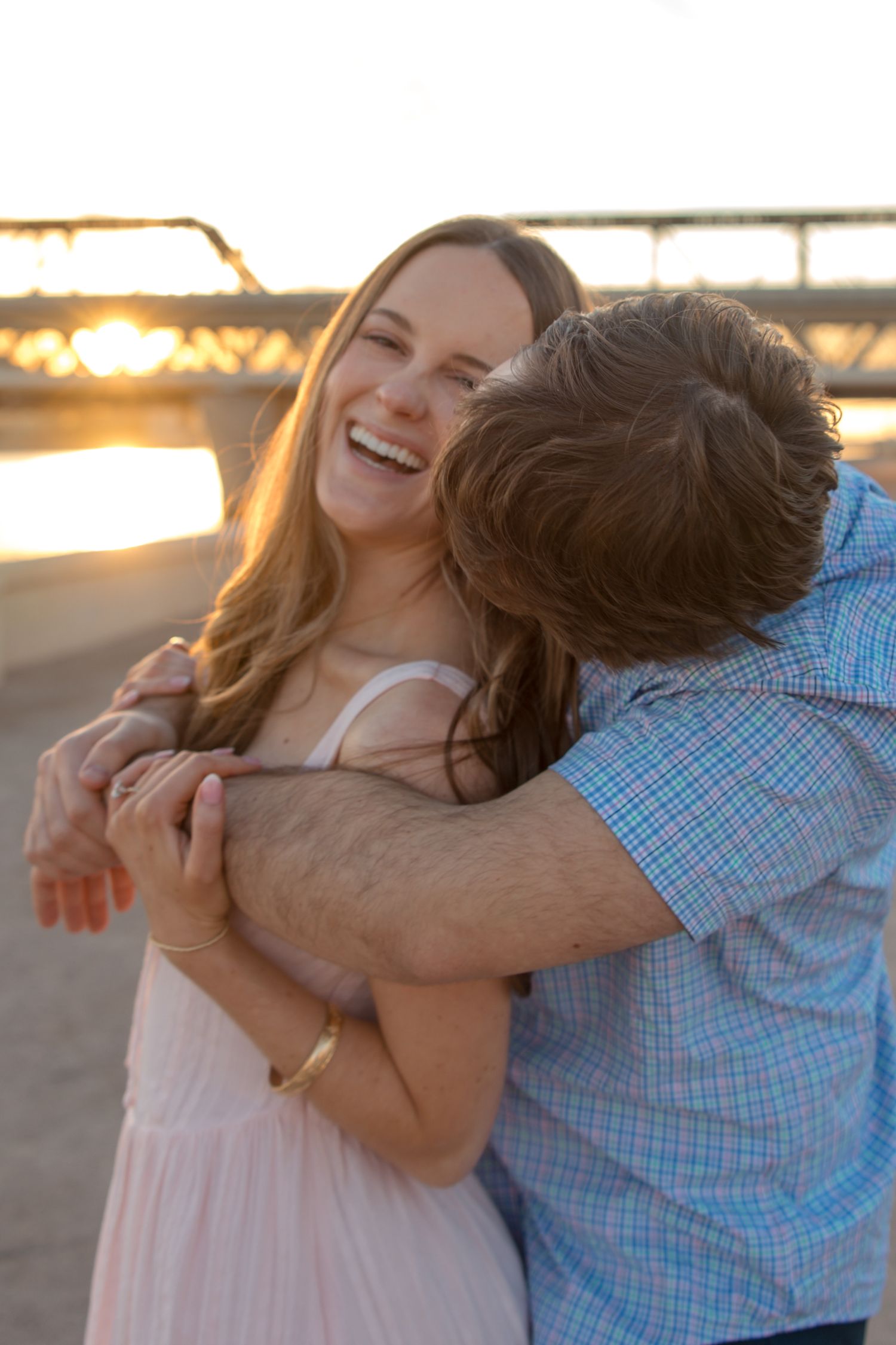 A laughing woman being embraced from behind by a man at sunset on a beach.