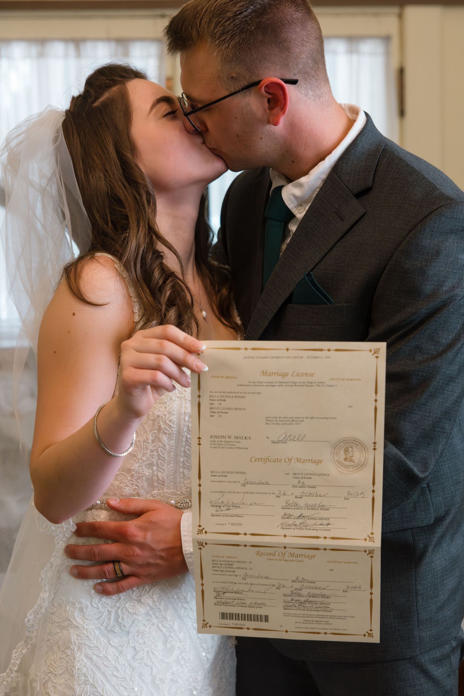 Newlyweds kiss while proudly displaying their official marriage certificate and license after the ceremony.