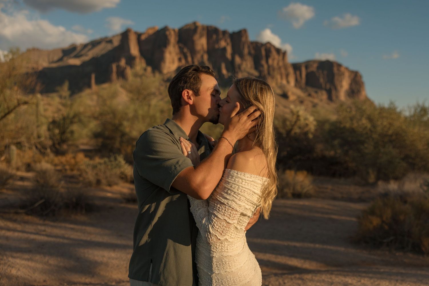Couple sharing a romantic kiss in the Arizona desert with Superstition Mountains in the golden hour background.