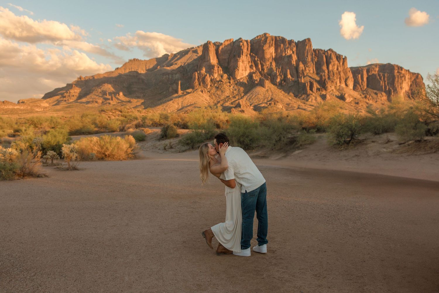 Couple sharing a romantic dip kiss in the Arizona desert with Superstition Mountains glowing at golden hour.