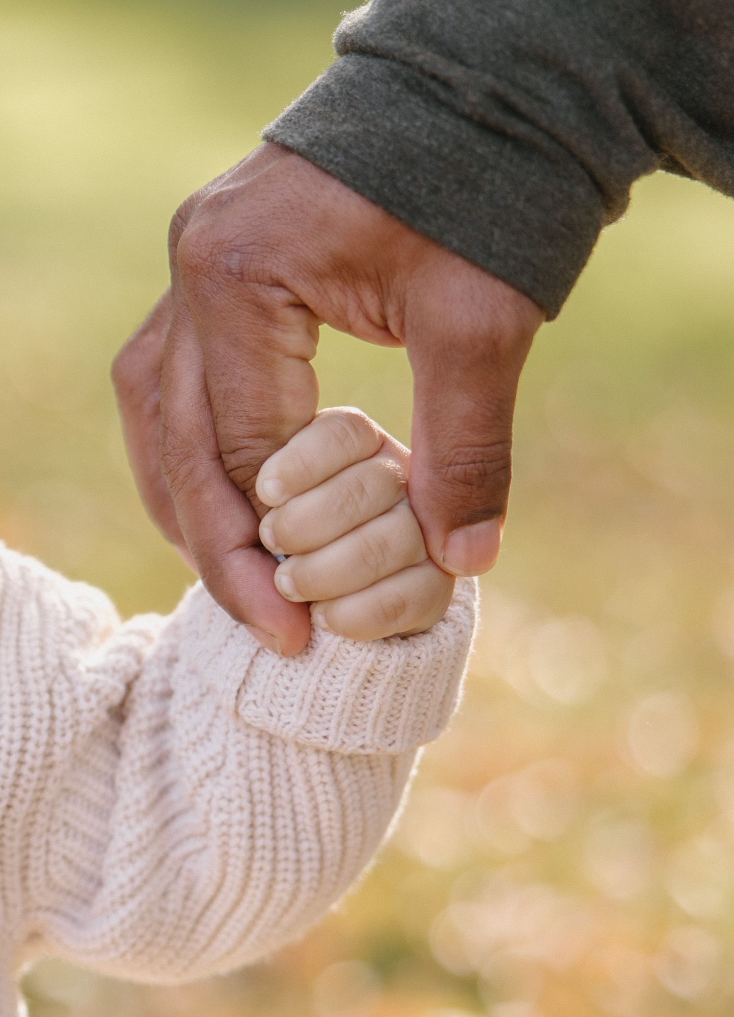 Adult hand gently holding a small child's fist outdoors, symbolizing love, trust, and family bonding.