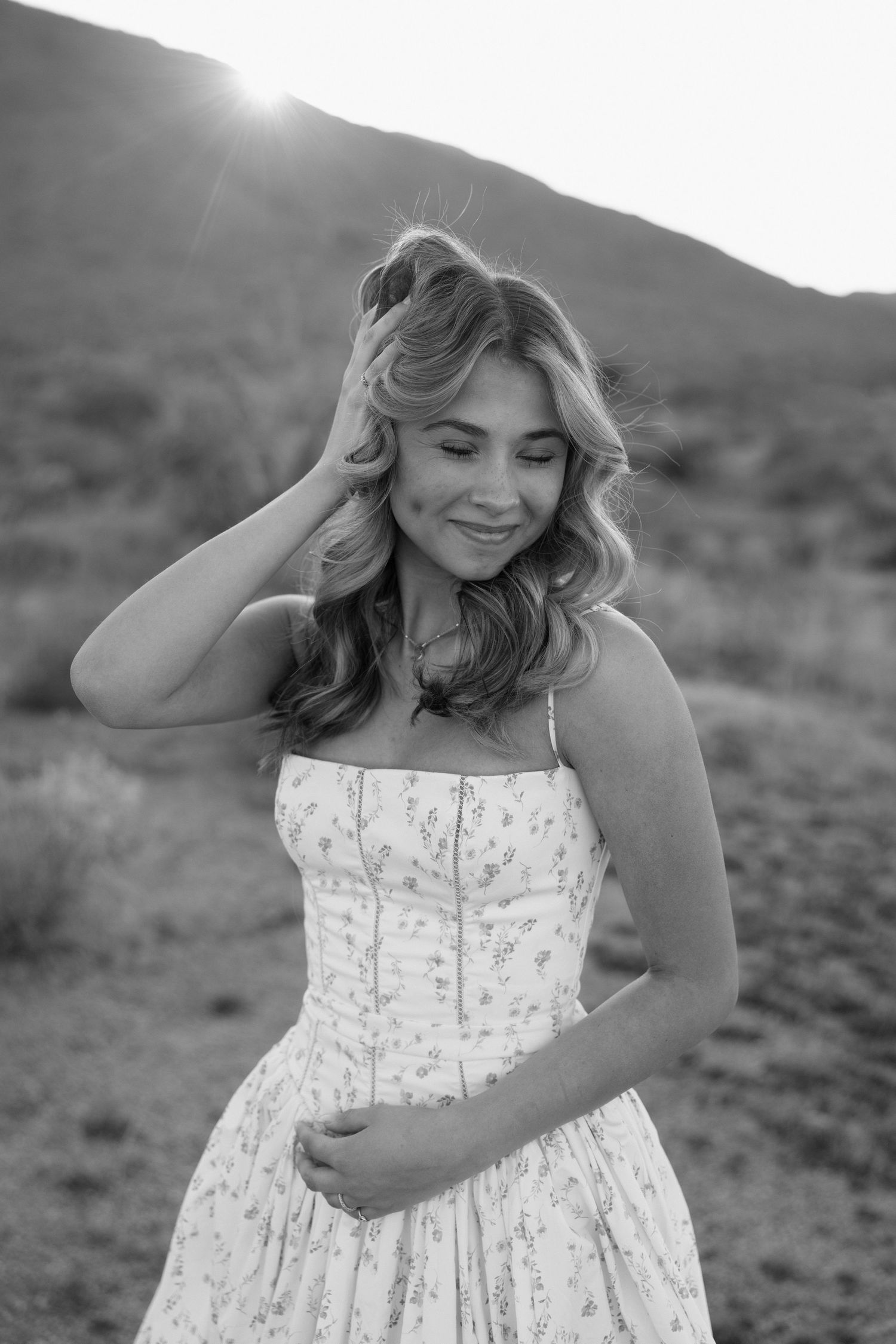 Black and white portrait of blonde woman in floral dress in desert landscape.