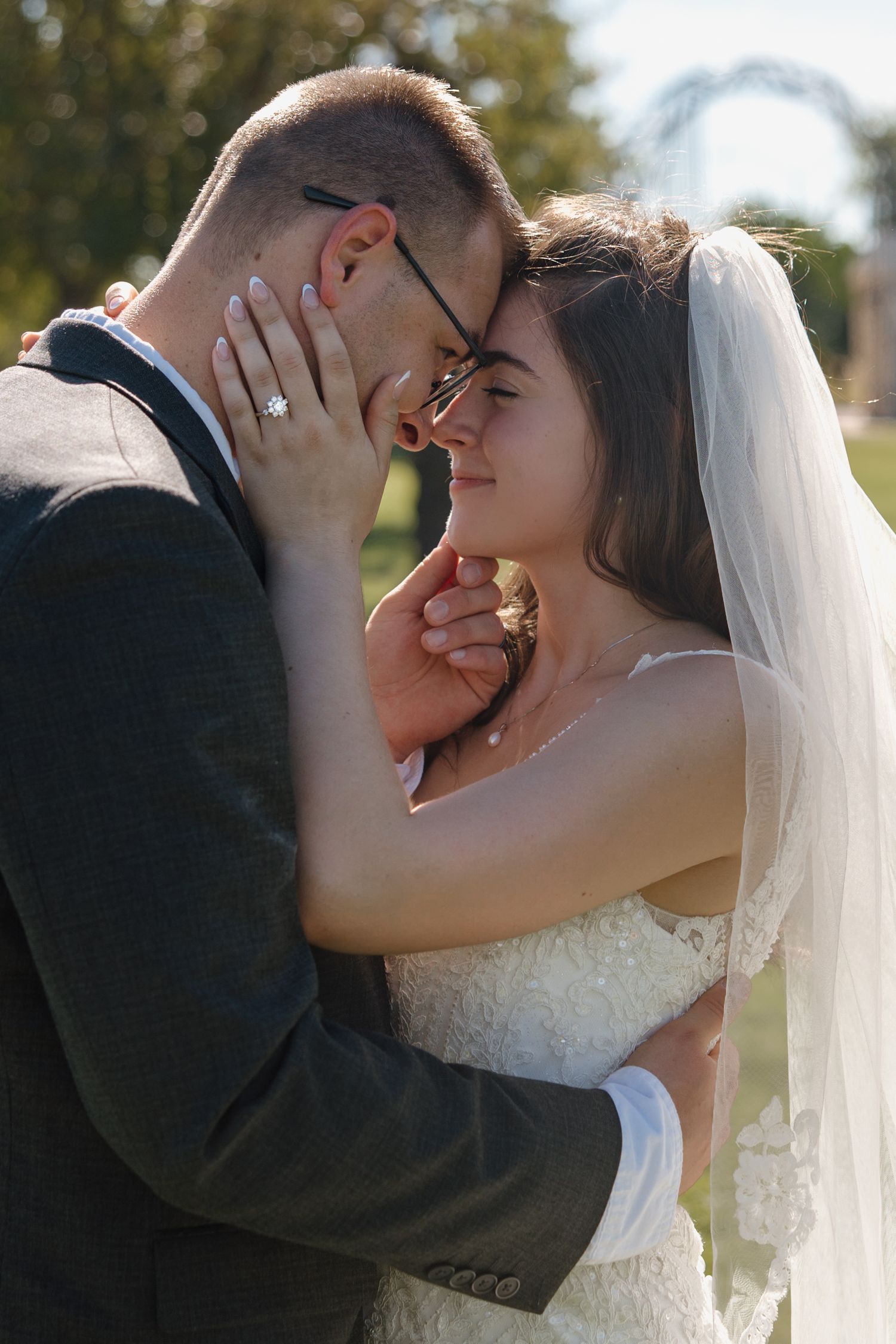Bride tenderly holds grooms face as they share an intimate moment outdoors on their wedding day.