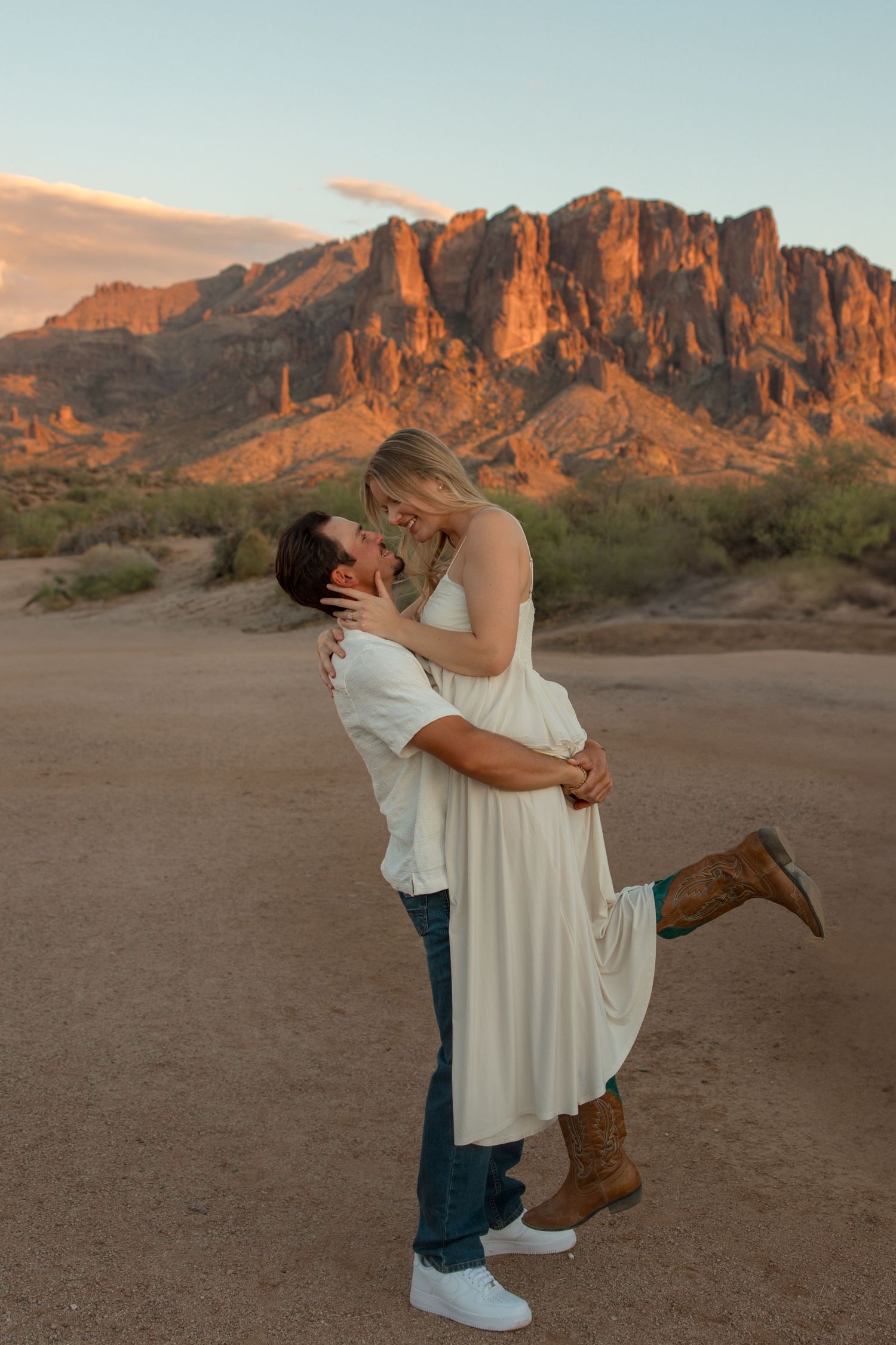 Couple sharing a romantic kiss at sunset with the Superstition Mountains glowing in the Arizona desert background.