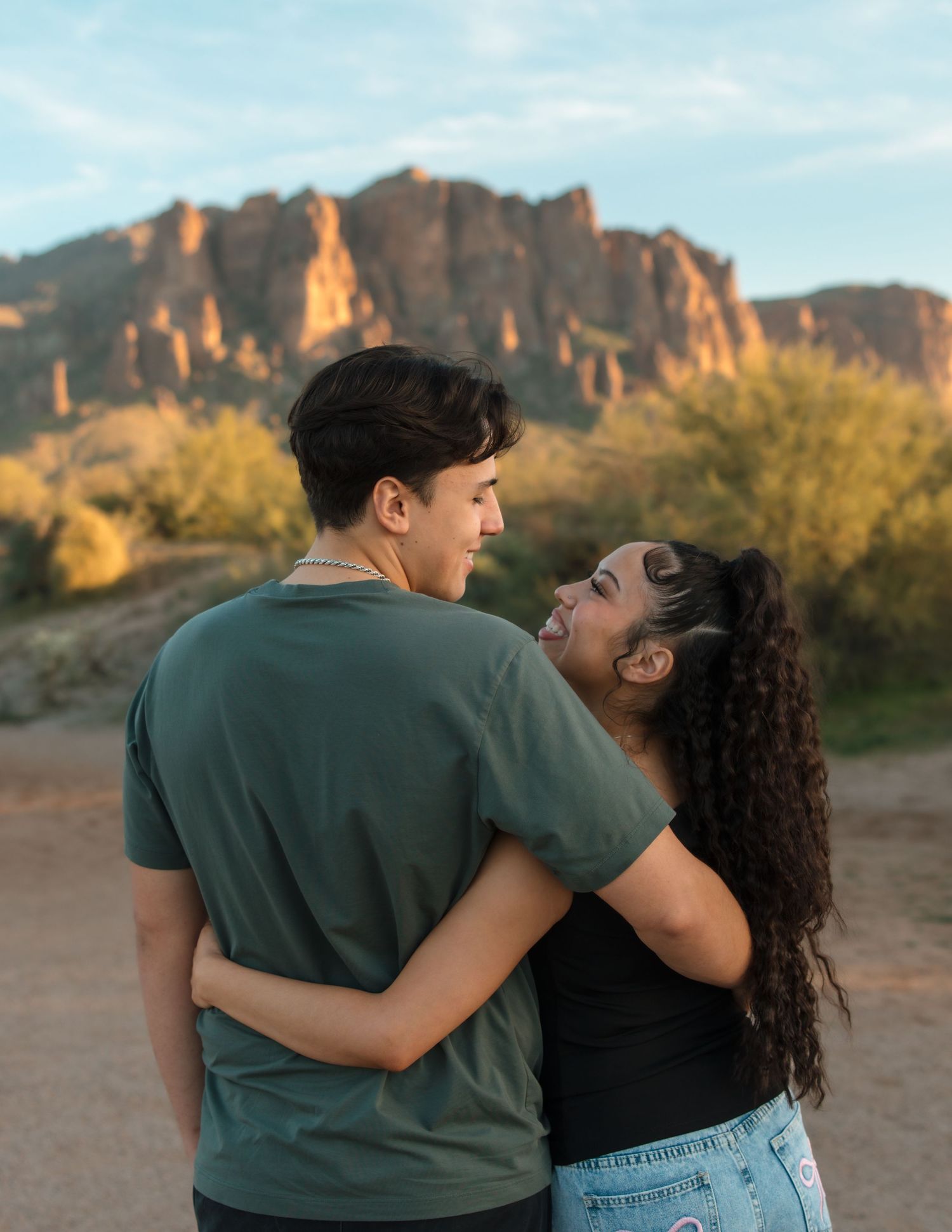 A couple embraces and smiles at each other with stunning desert rock formations in the background.