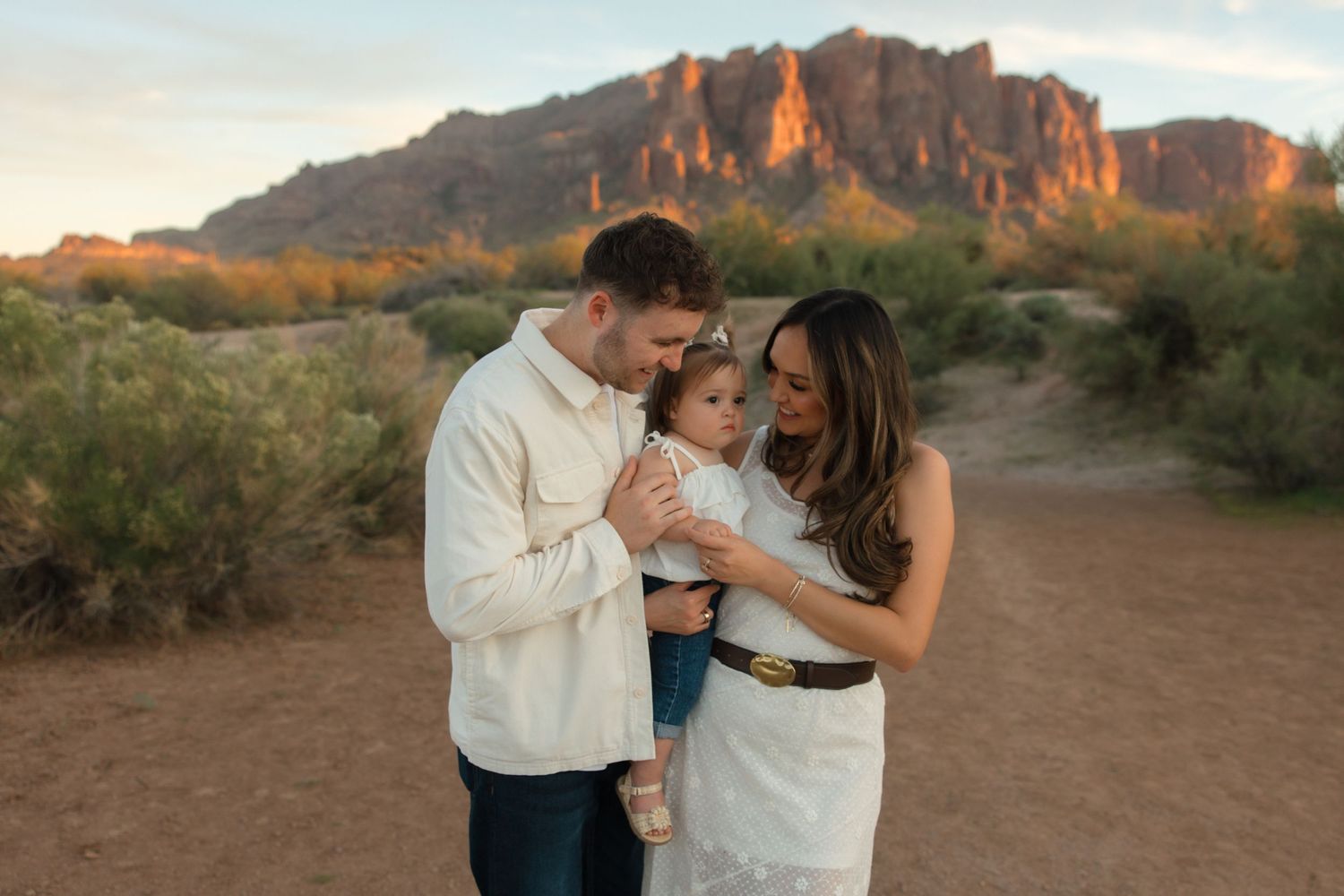 Family of three sharing a tender moment in the Arizona desert with Superstition Mountains glowing at golden hour.