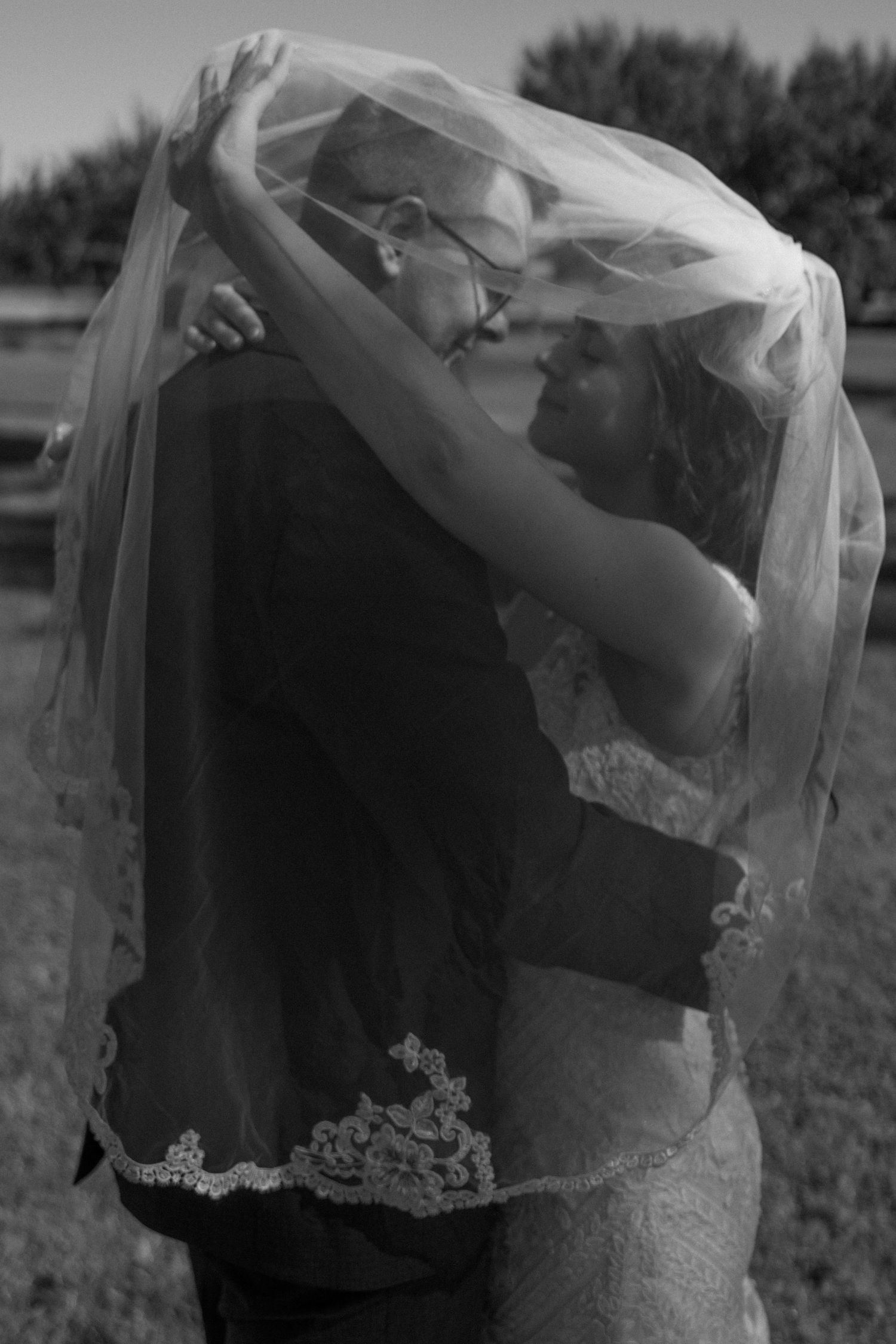Black and white romantic photo of bride and groom sharing an intimate moment under the bridal veil outdoors.