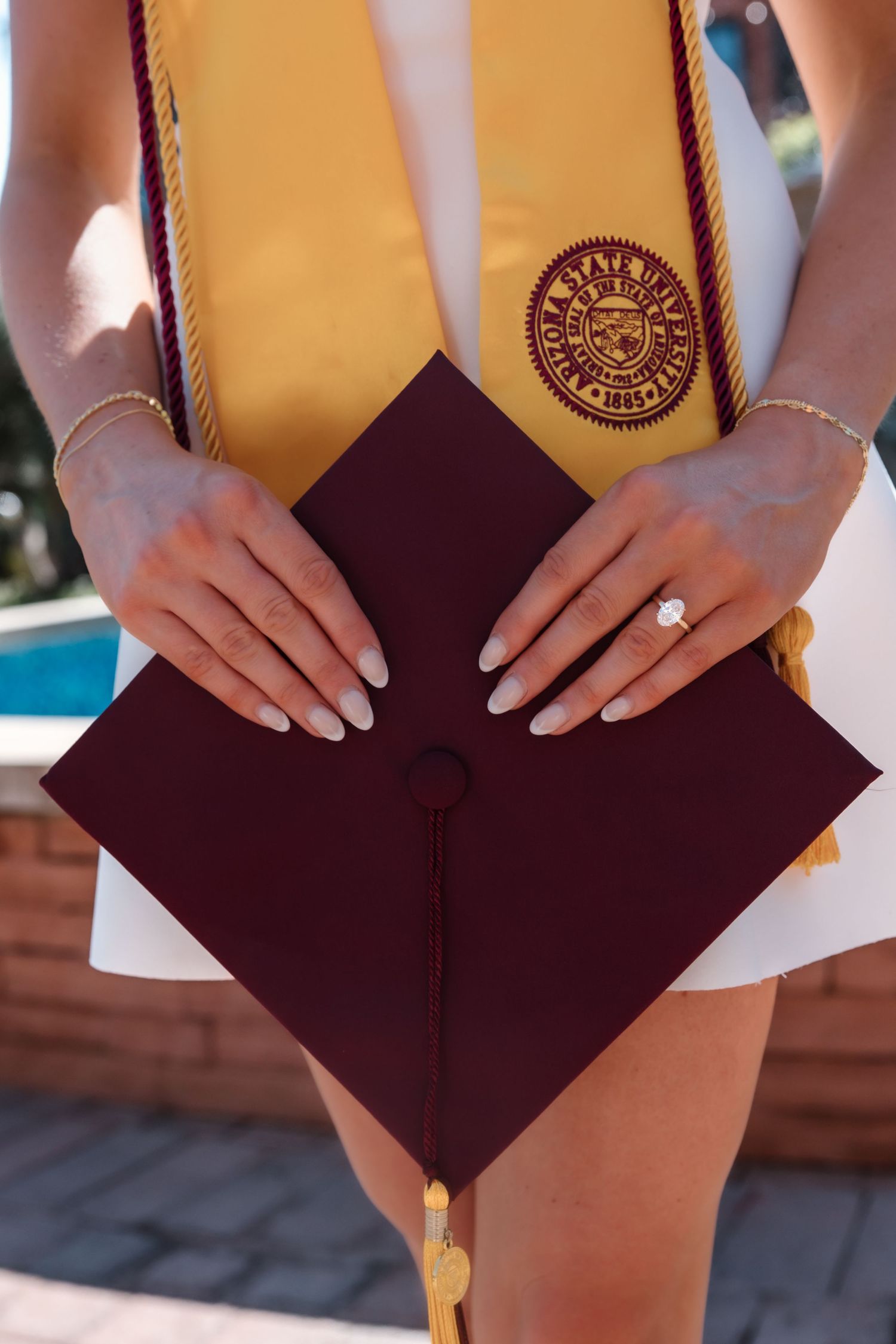 Close-up of ASU graduation cap and gold stole with university seal held by female graduate.
