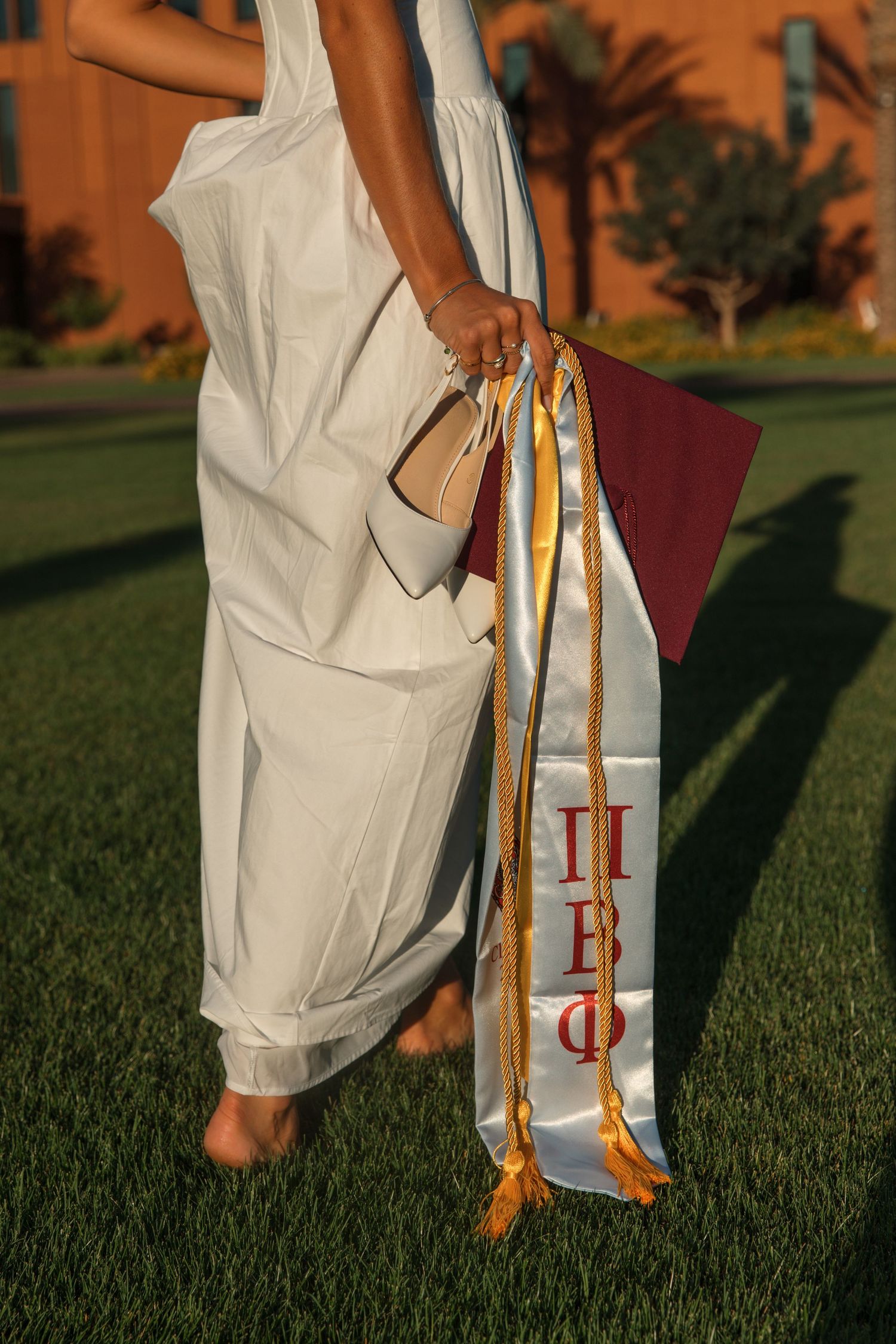 Close-up of graduate holding maroon cap and Pi Beta Phi sorority stole on grass.