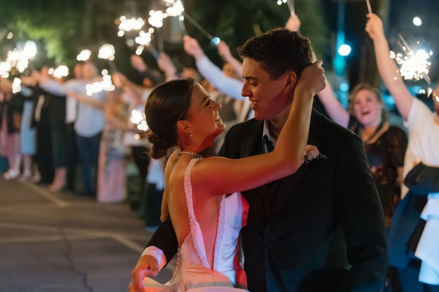 Bride and groom share a joyful dance during sparkler sendoff with cheering guests lining the path at night.