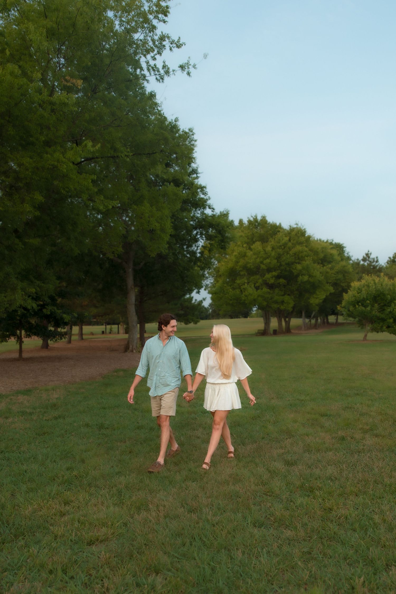 Young couple holding hands walking through a green park at dusk.