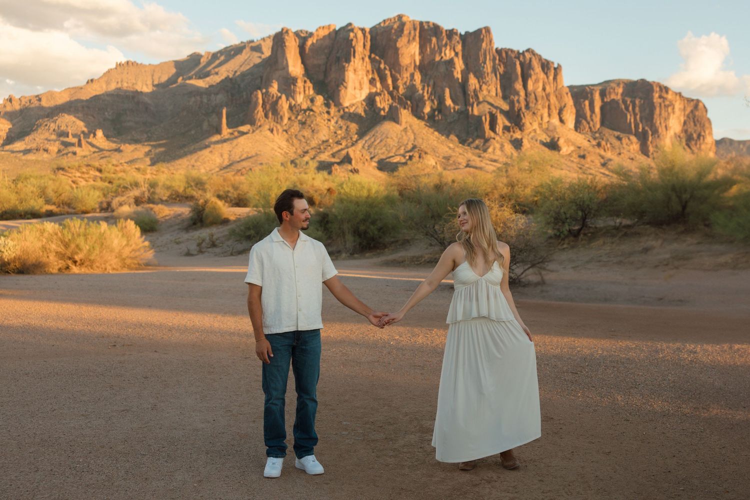 Couple holding hands in desert landscape with Superstition Mountains at golden hour in Arizona.