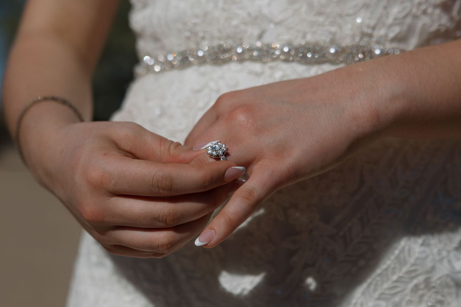 Close-up of bride's hands showcasing elegant diamond engagement ring against lace wedding dress.