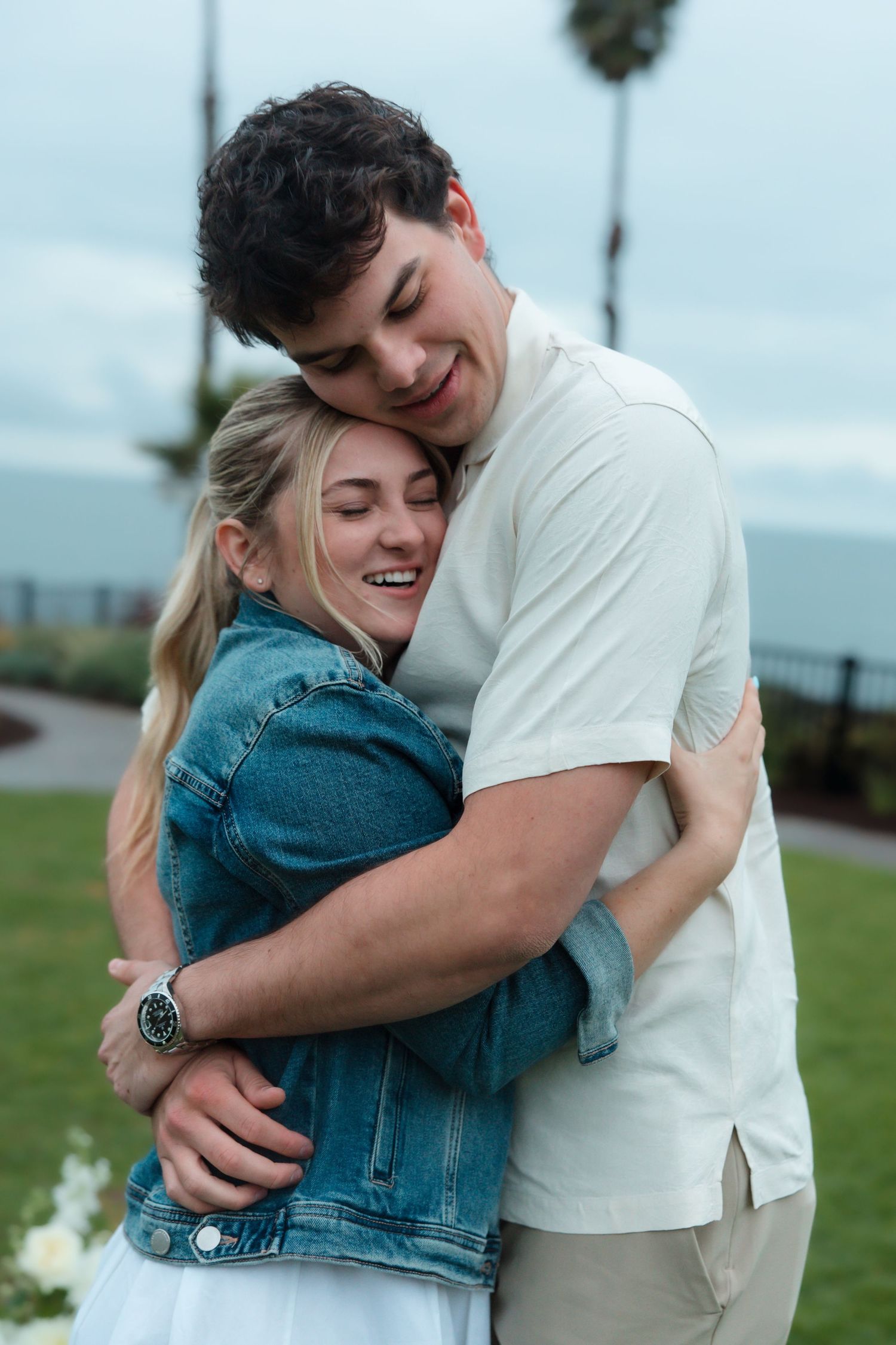 Happy couple embracing and laughing outdoors near ocean with palm trees in background.