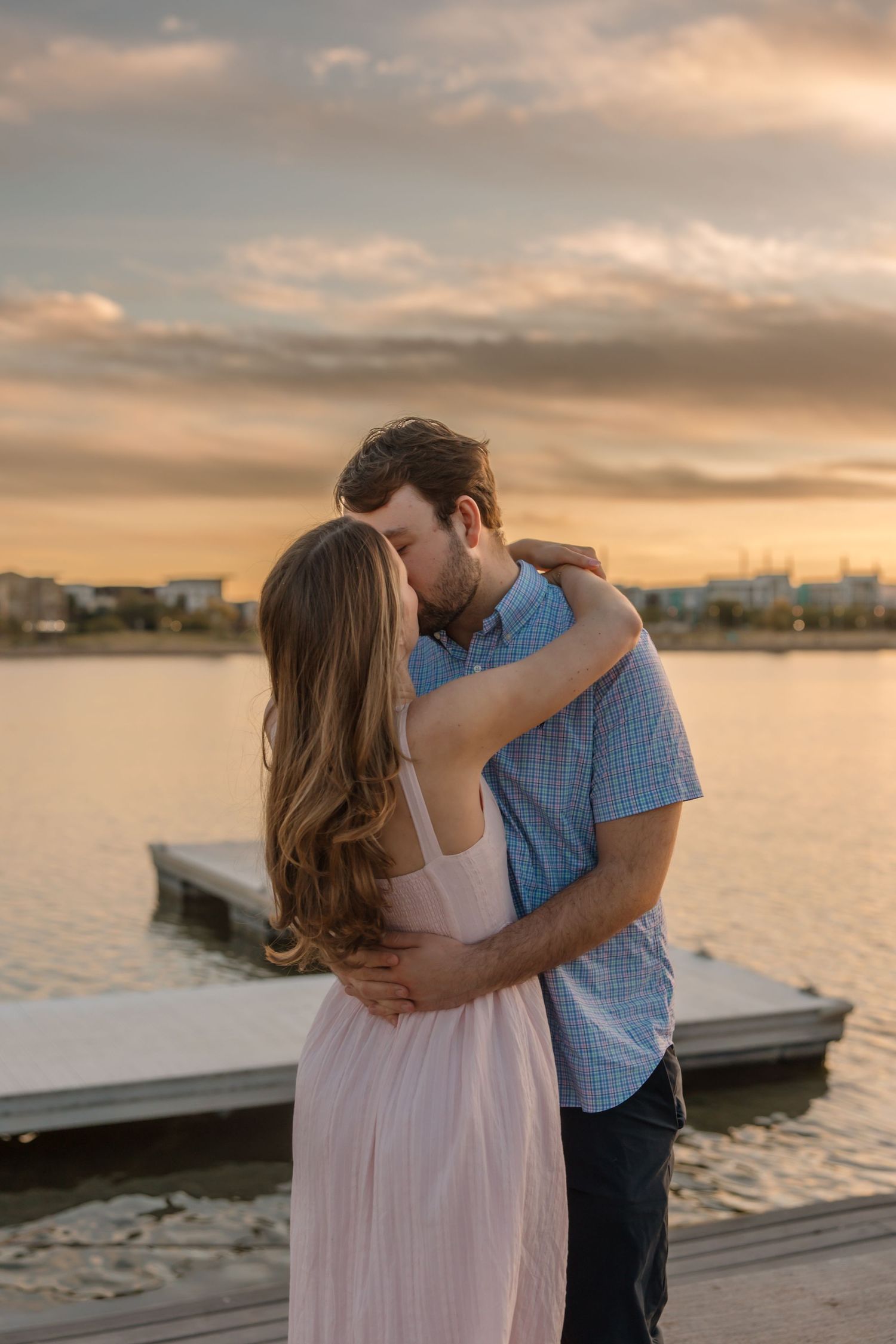 Couple embracing and kissing near a waterfront dock during a breathtaking golden sunset outdoors.