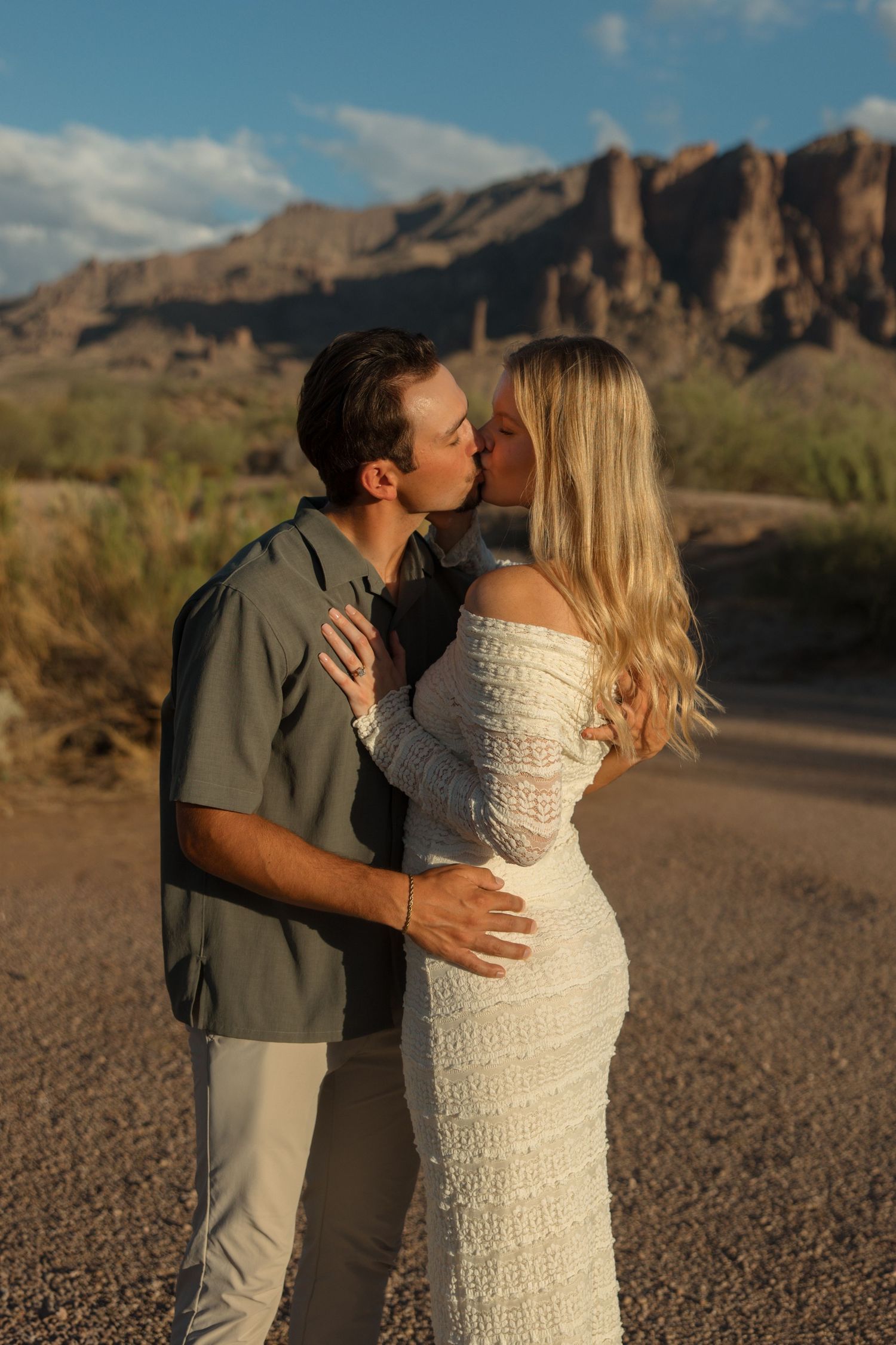 Couple sharing a romantic kiss in the Arizona desert with rugged mountain backdrop at golden hour.