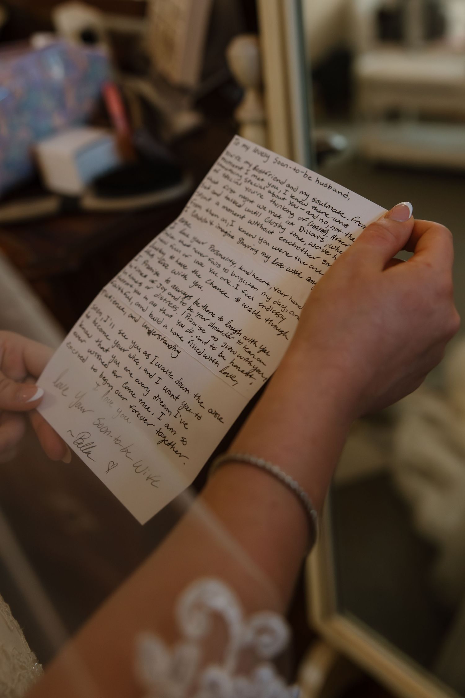 Close-up of bride holding handwritten wedding letter with lace dress and diamond bracelet visible.