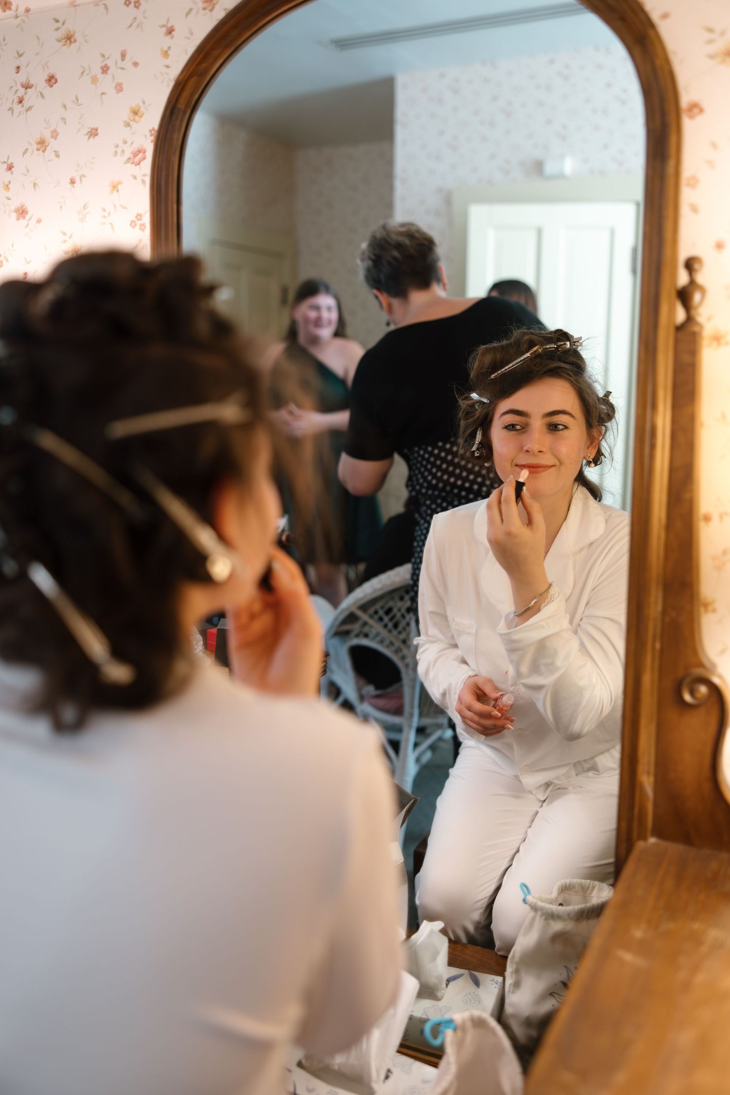 Bride applying lipstick while seated at a vintage mirror during wedding preparations.