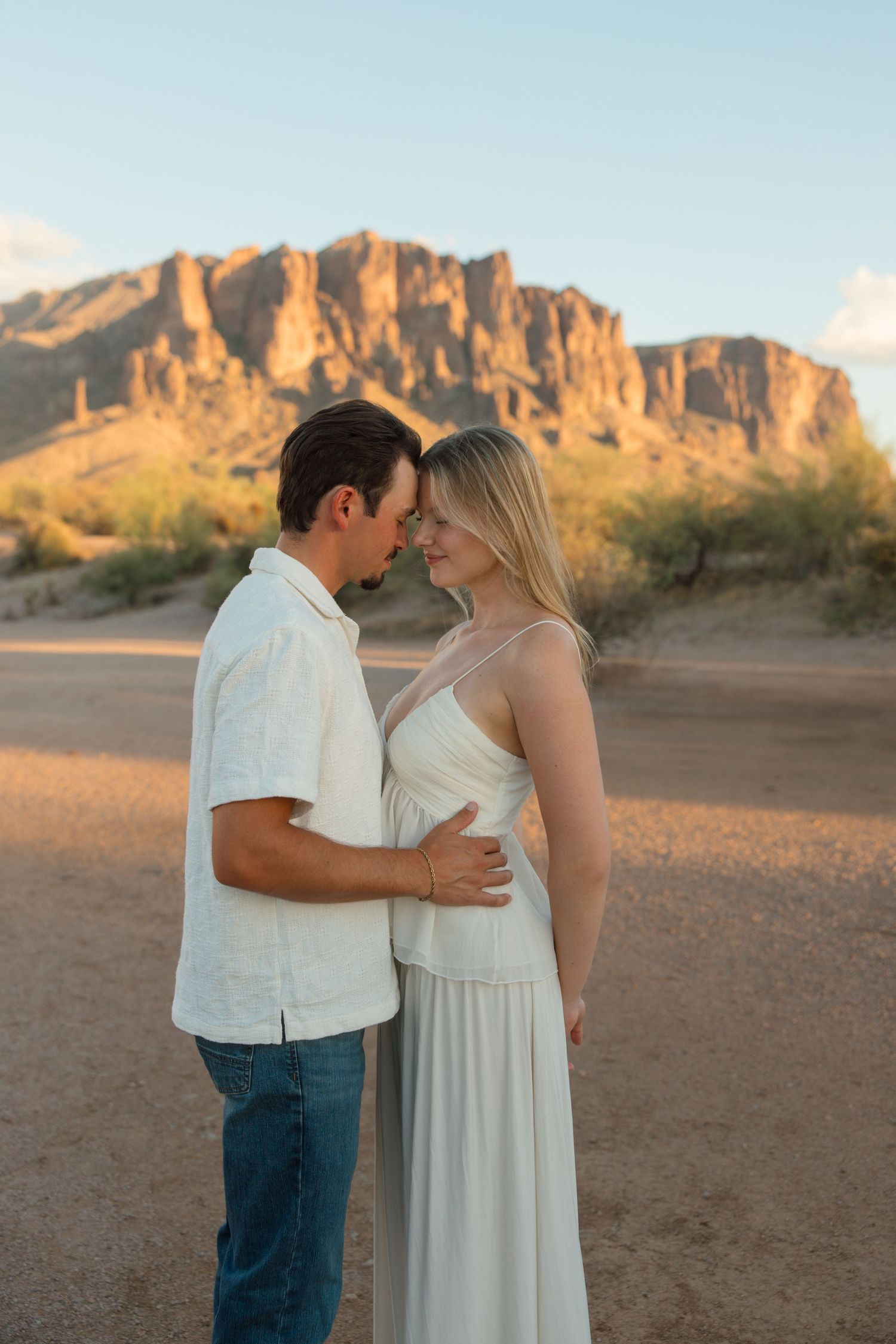 Romantic couple holding each other close at golden hour with Superstition Mountains in background.