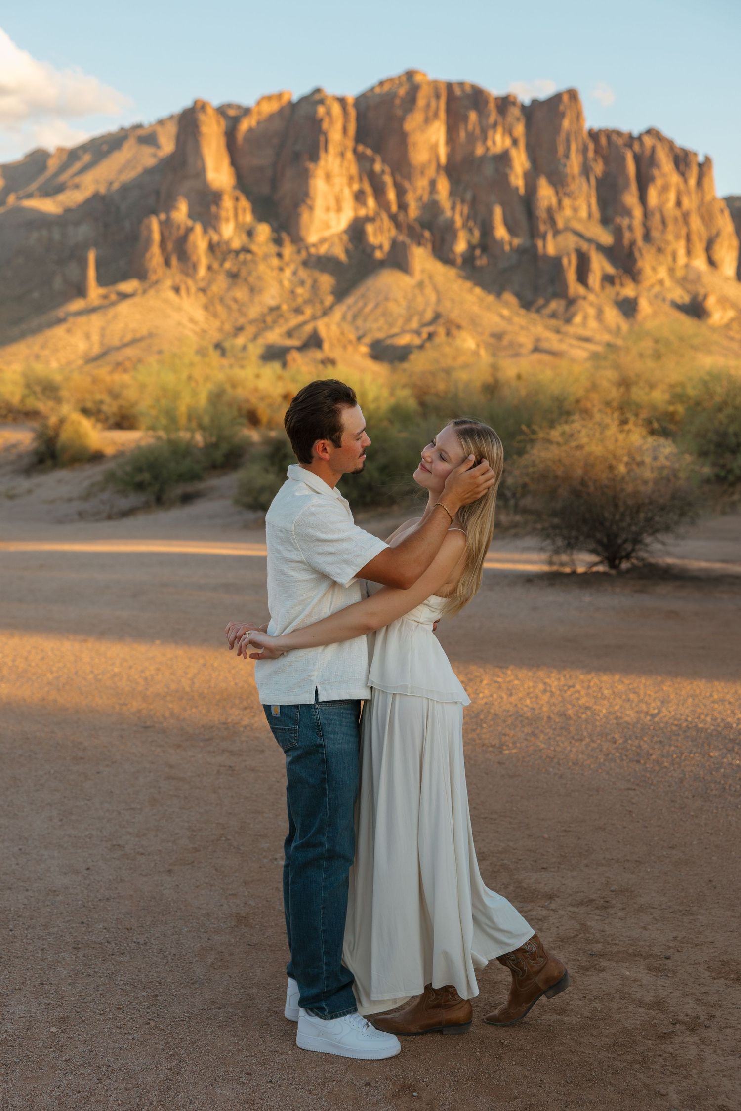 Couple embracing at golden hour in Arizona desert with Superstition Mountains backdrop.