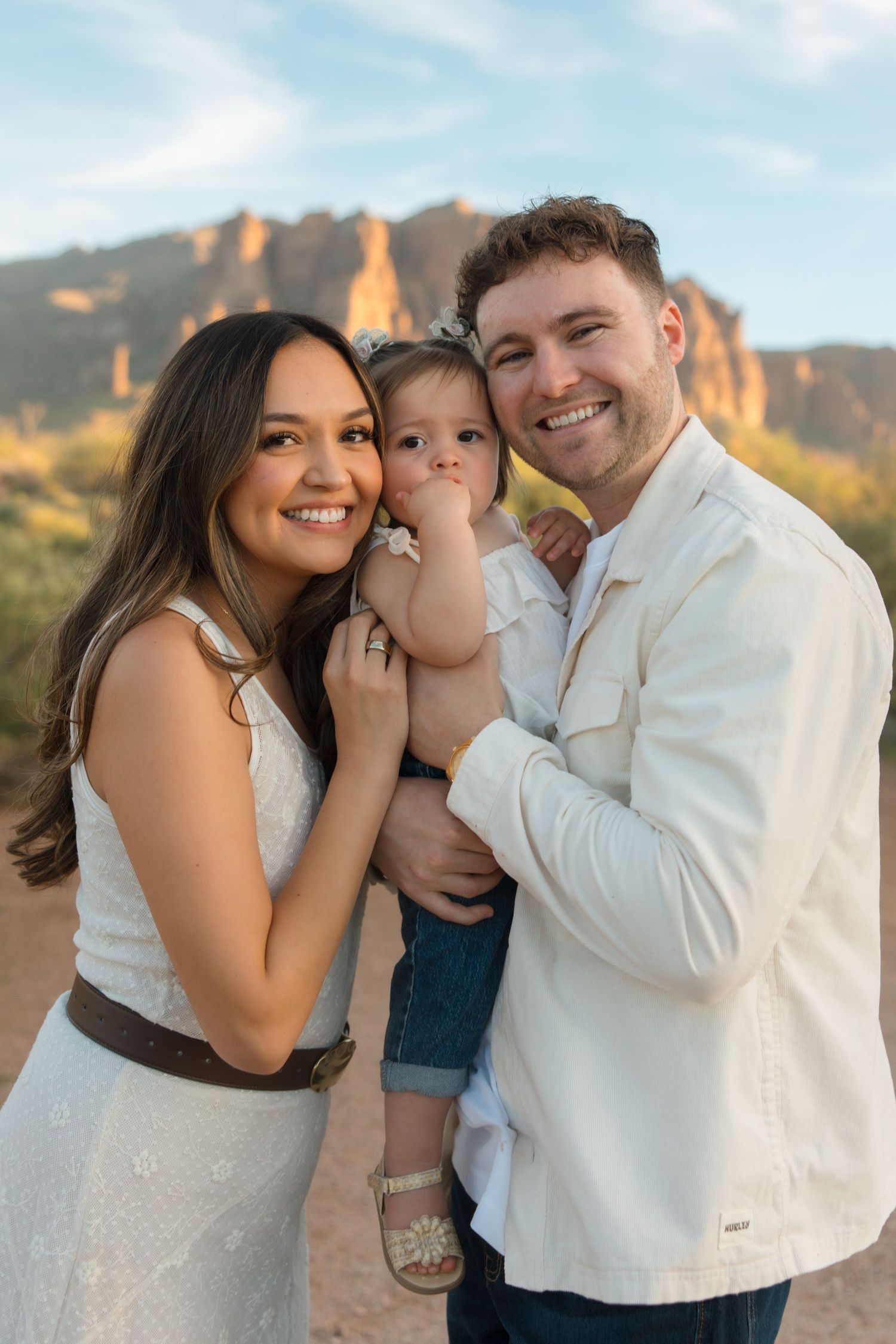 Happy young family with baby posing outdoors near desert rock formations in Arizona during golden hour.