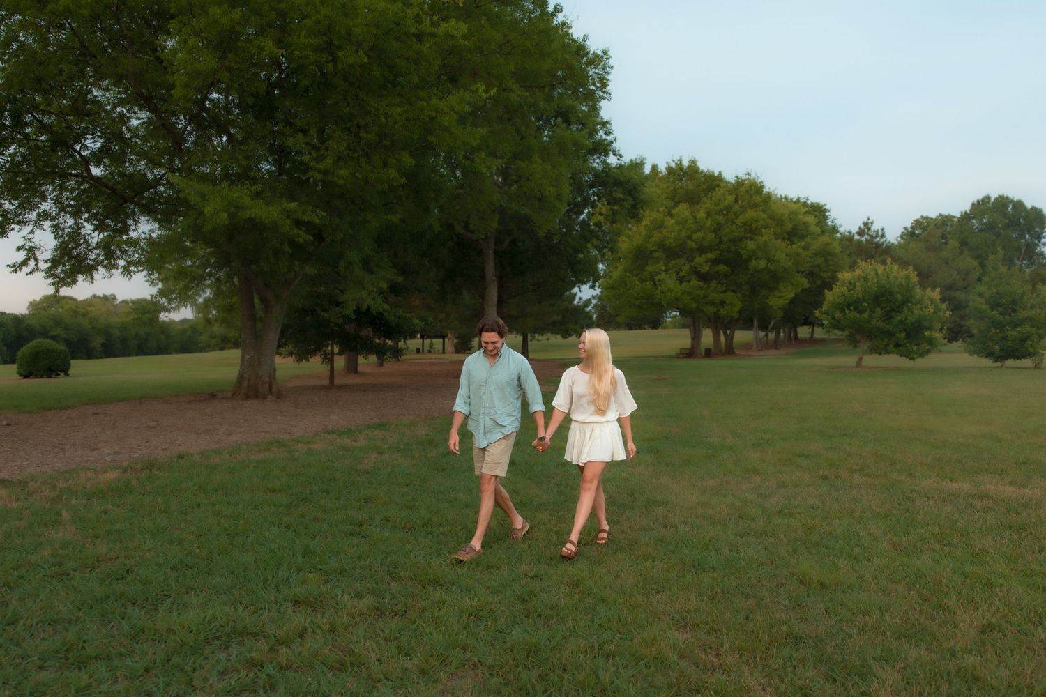 Happy couple strolling hand in hand across a grassy park at sunset.