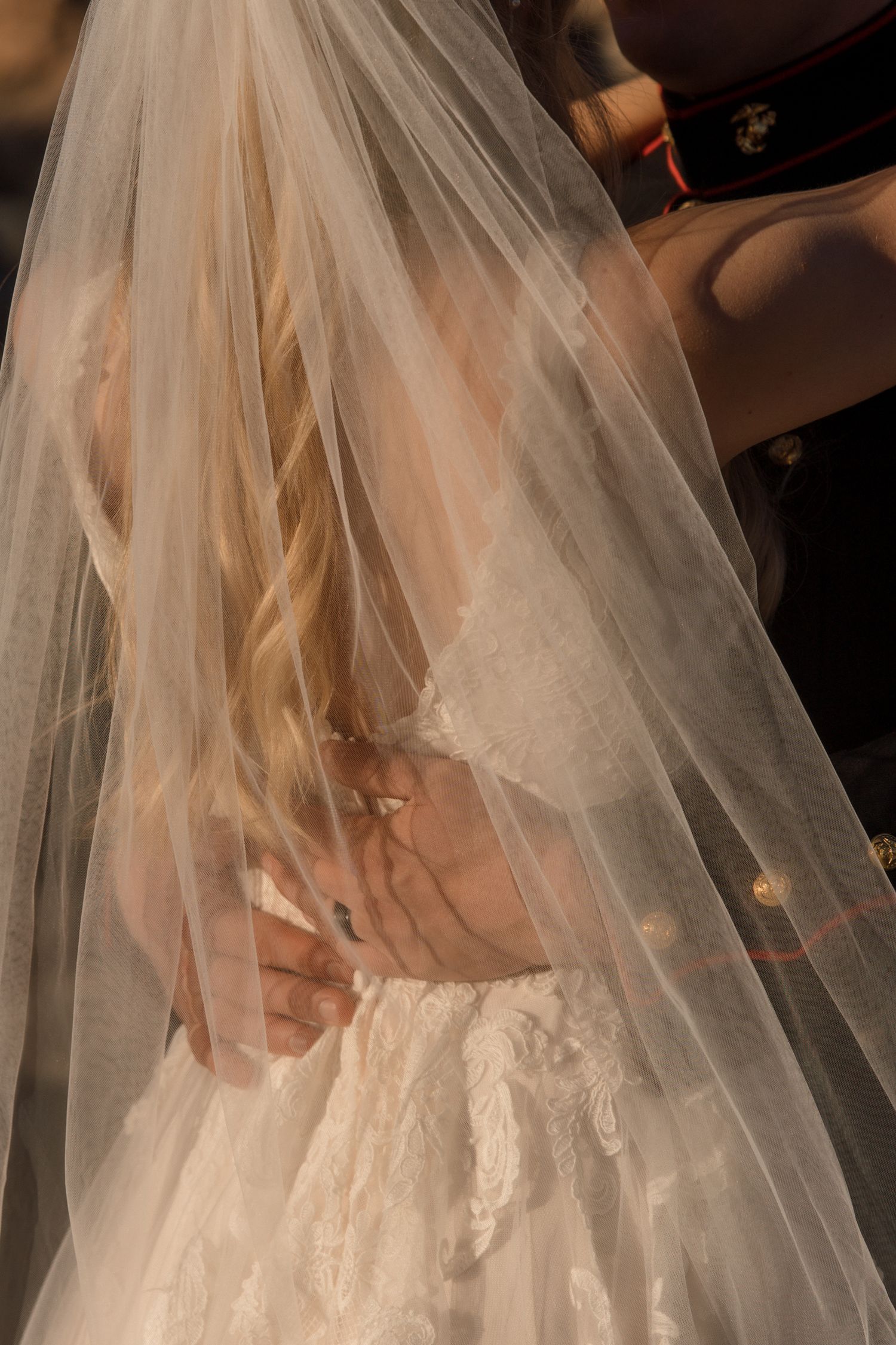 Close-up of Marine groom embracing bride, her flowing white veil cascading over lace wedding dress.