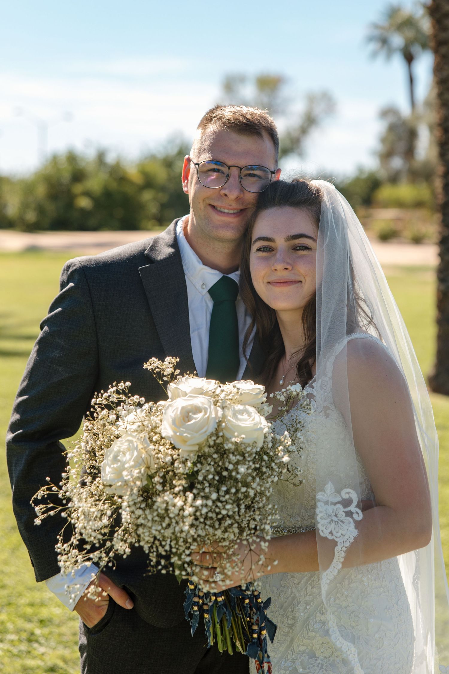 Smiling bride and groom portrait outdoors, bride holding white rose and baby's breath bouquet.