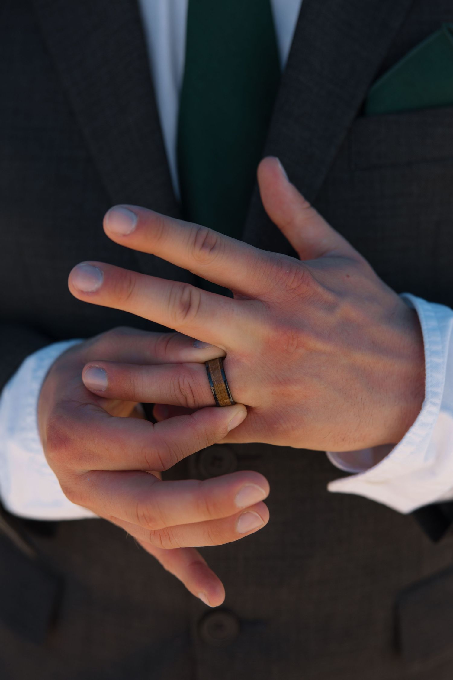 Close-up of groom adjusting wooden wedding band on his finger in a dark suit.
