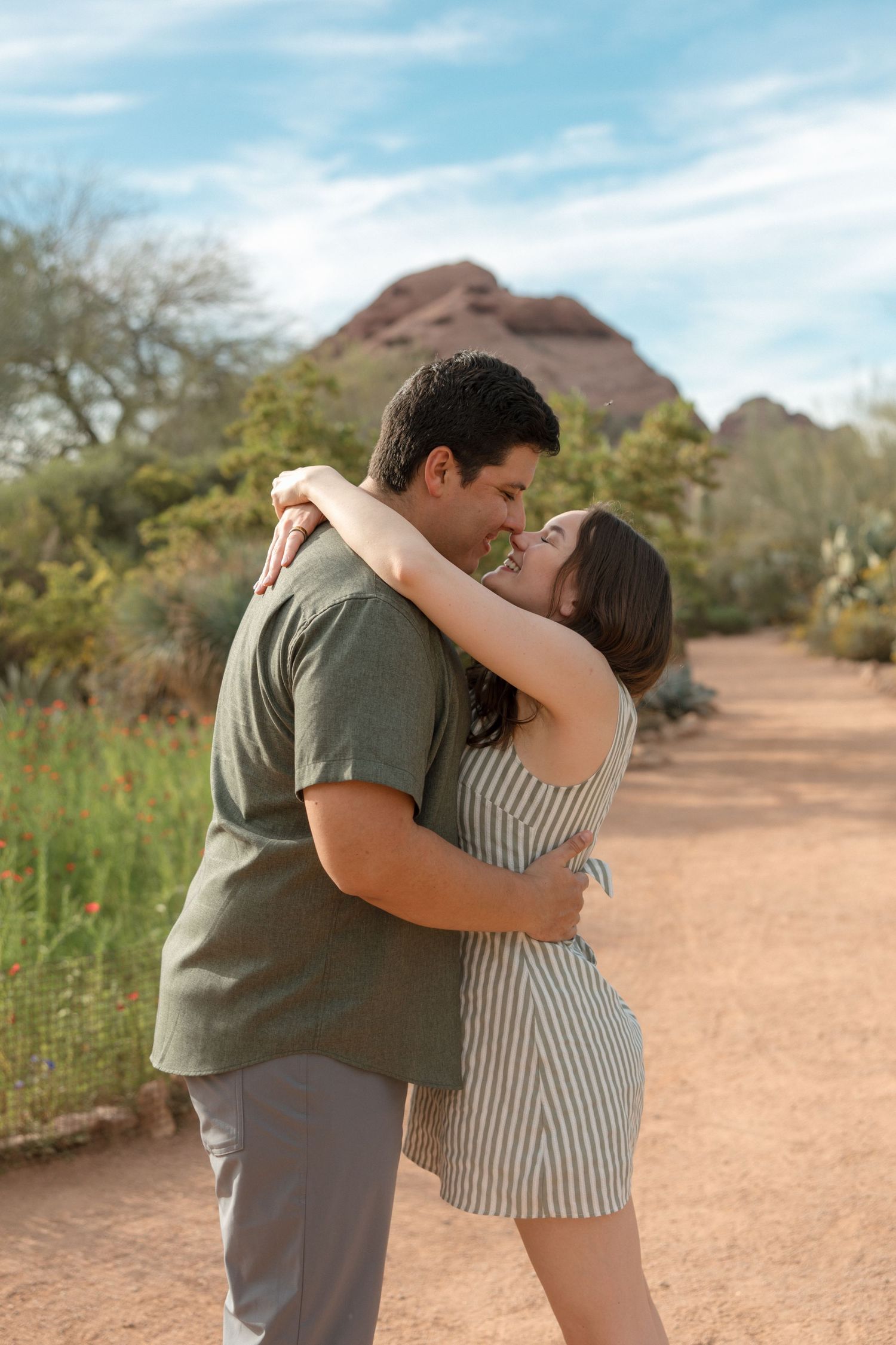 Happy couple embracing and smiling at each other on a desert trail with red rock mountains in the background.