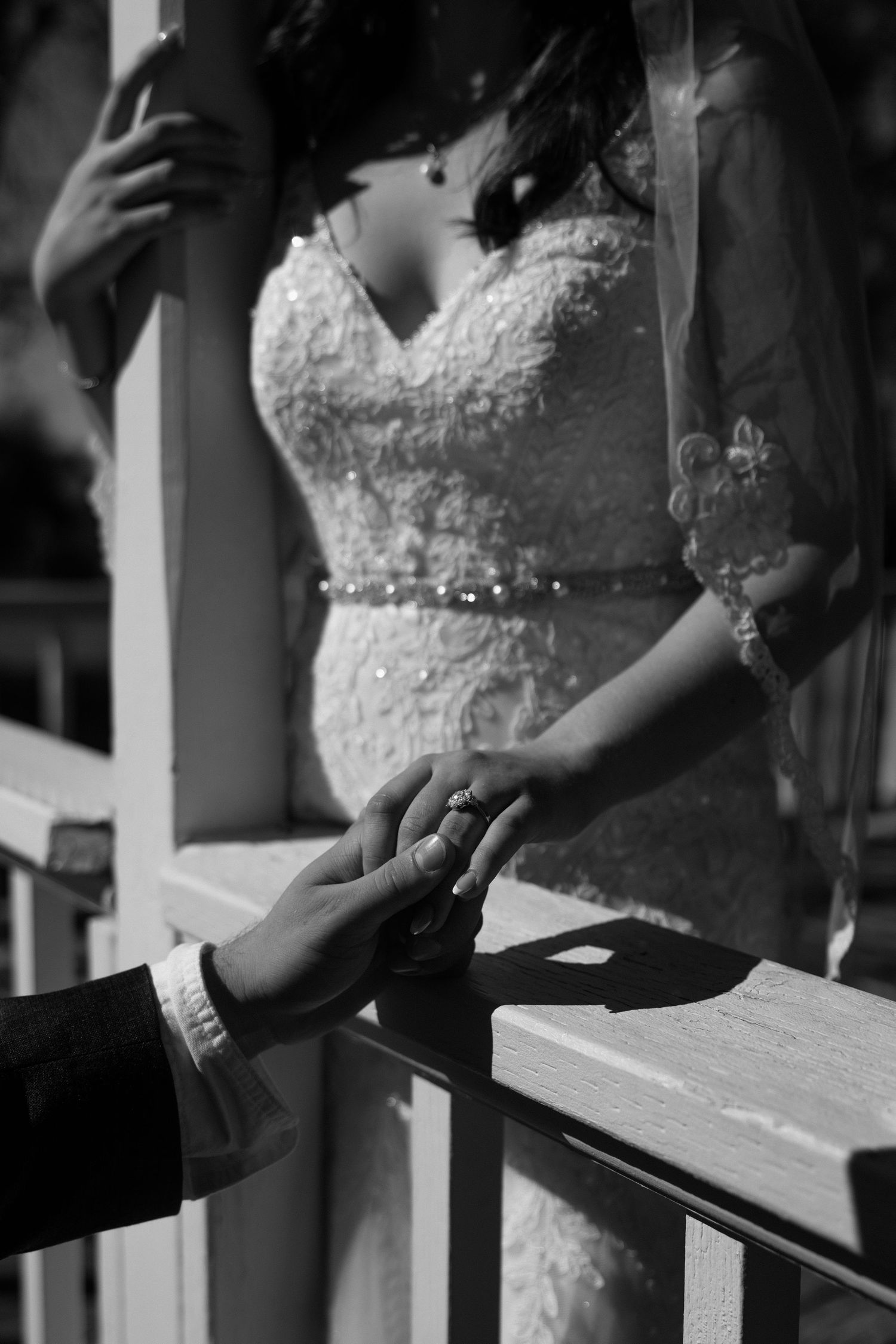 Black and white photo of groom holding brides hand during wedding ring exchange ceremony in elegant lace gown.