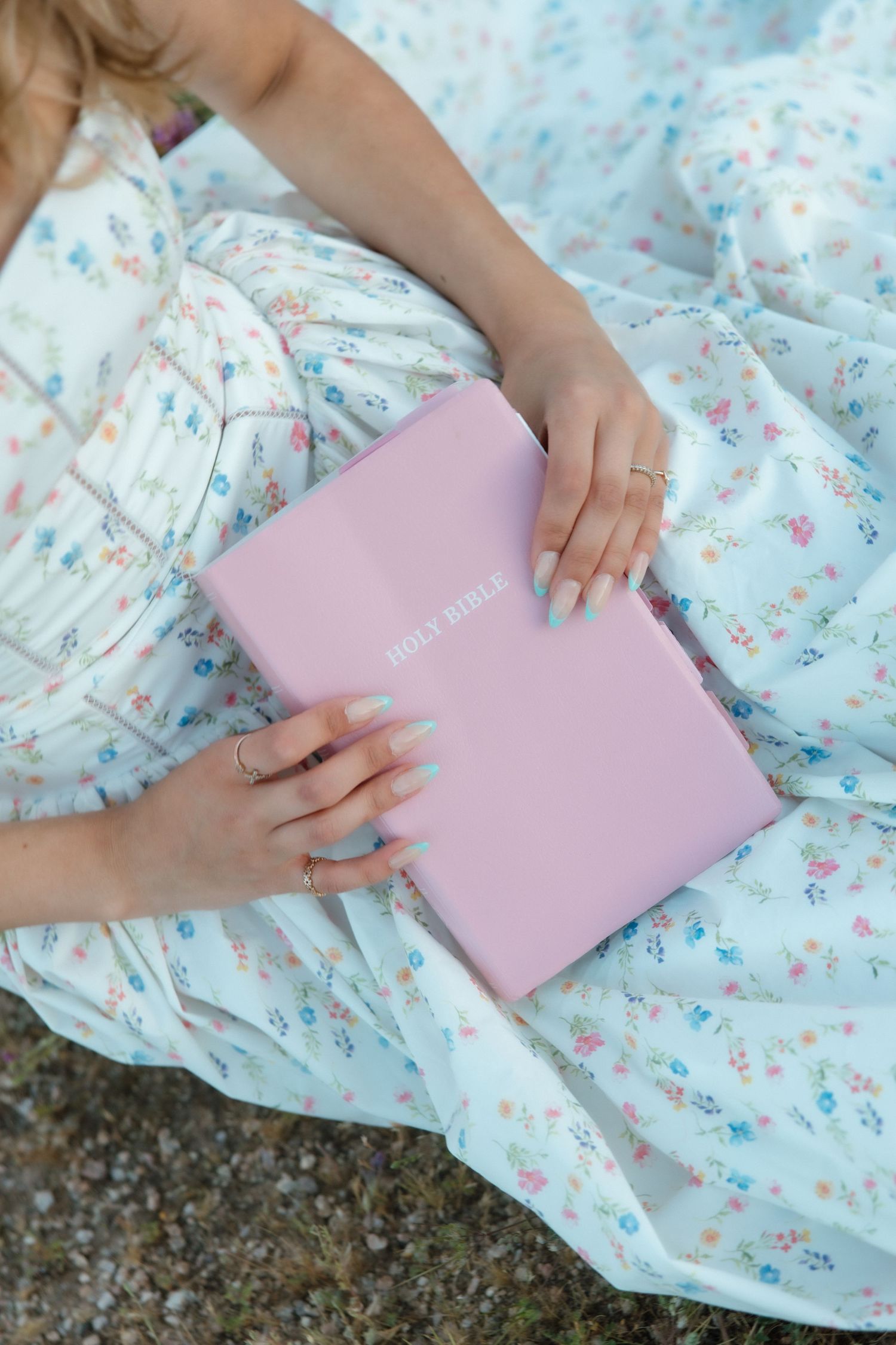 Woman in floral dress holding a pink Holy Bible outdoors.