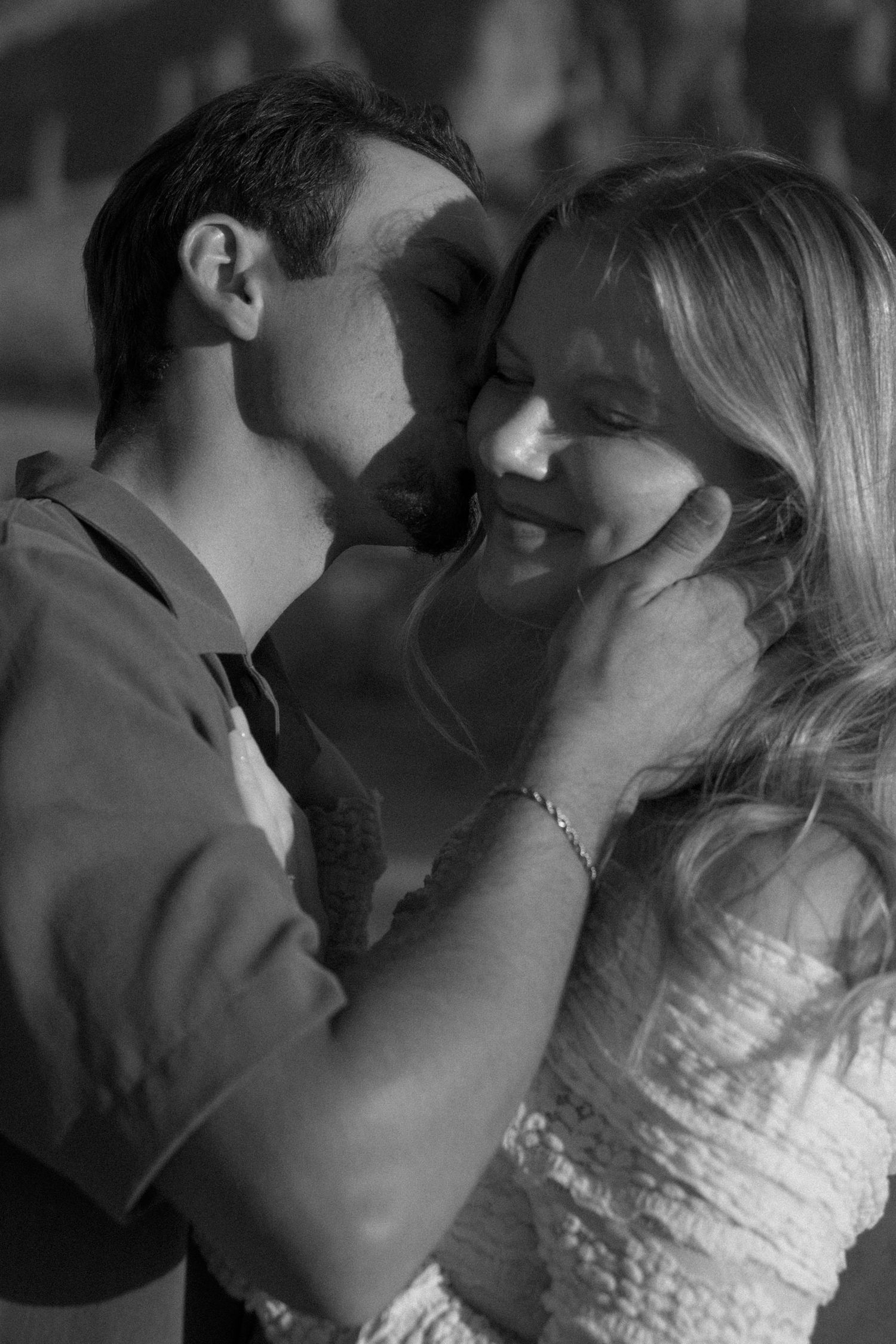 Black and white photo of a romantic couple embracing, man gently holding woman's face as they share a tender moment.