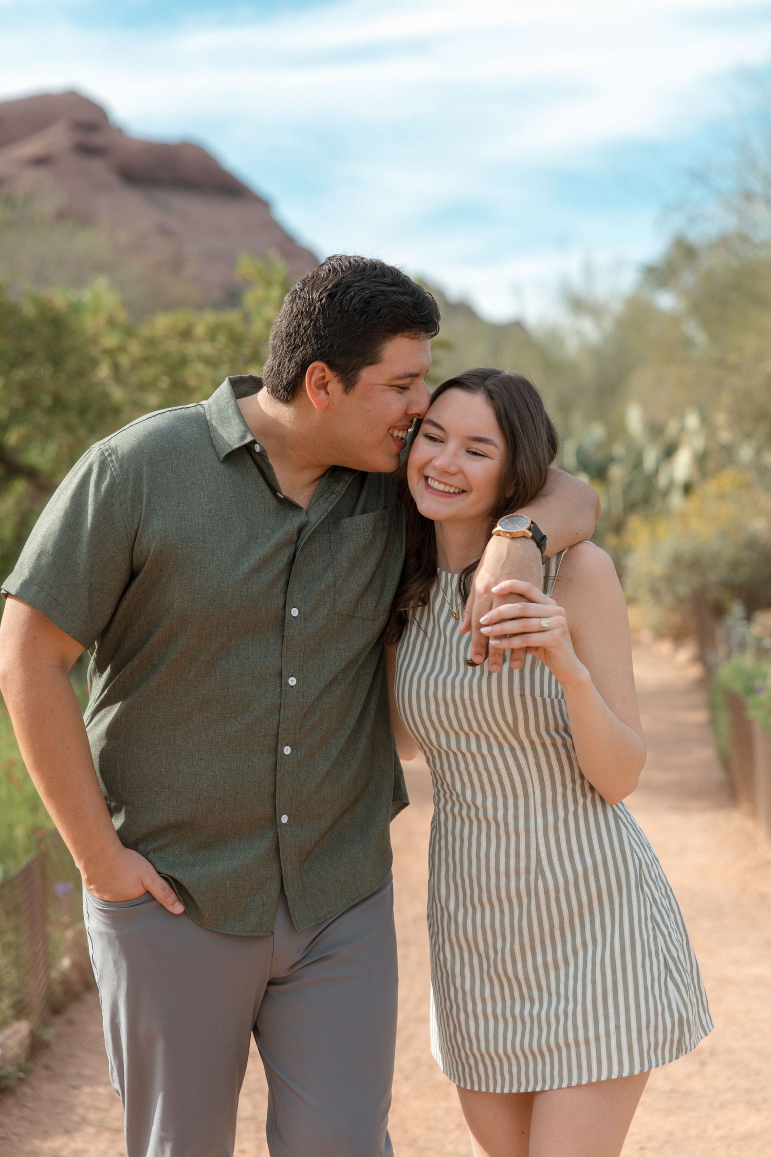 Happy couple embracing and walking on a desert path with red rock mountains in the background.